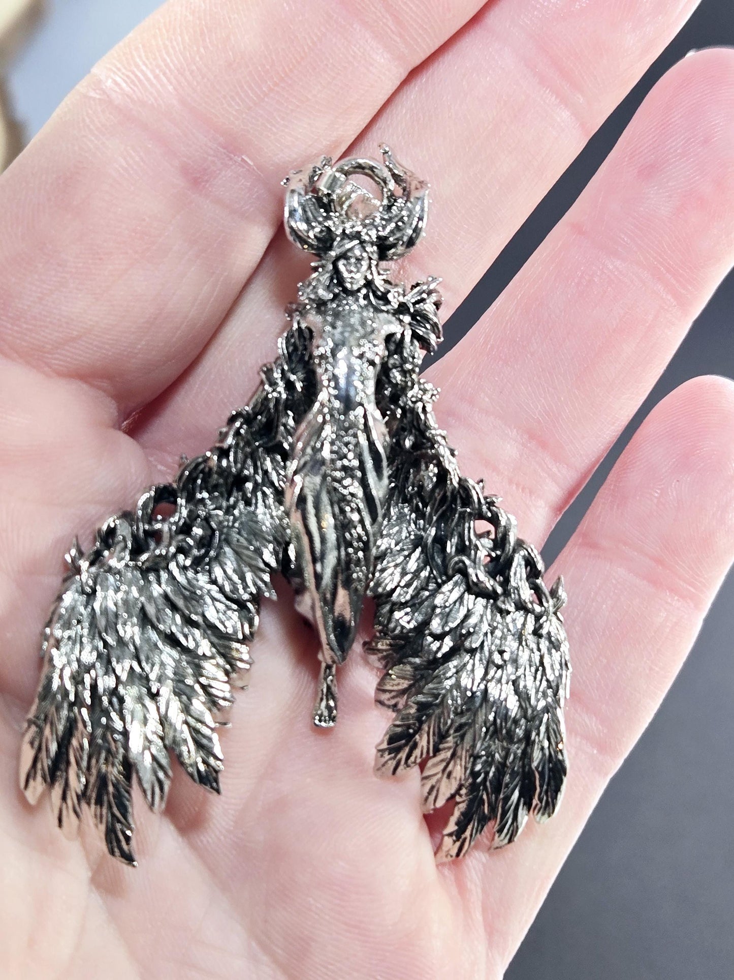 A hand holding a silver, intricately designed bird-shaped pendant or brooch.