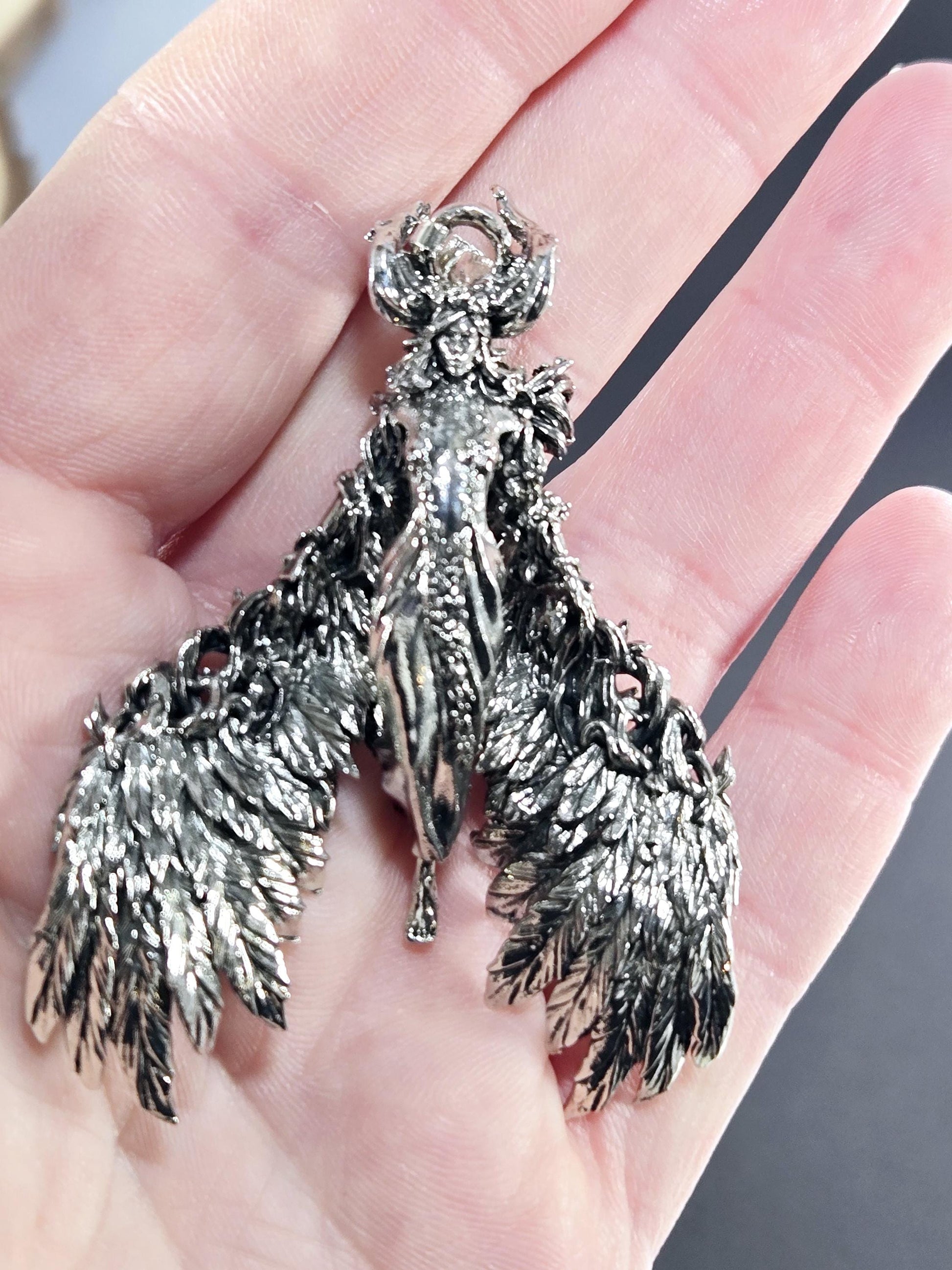 A hand holding a silver, intricately designed bird-shaped pendant or brooch.