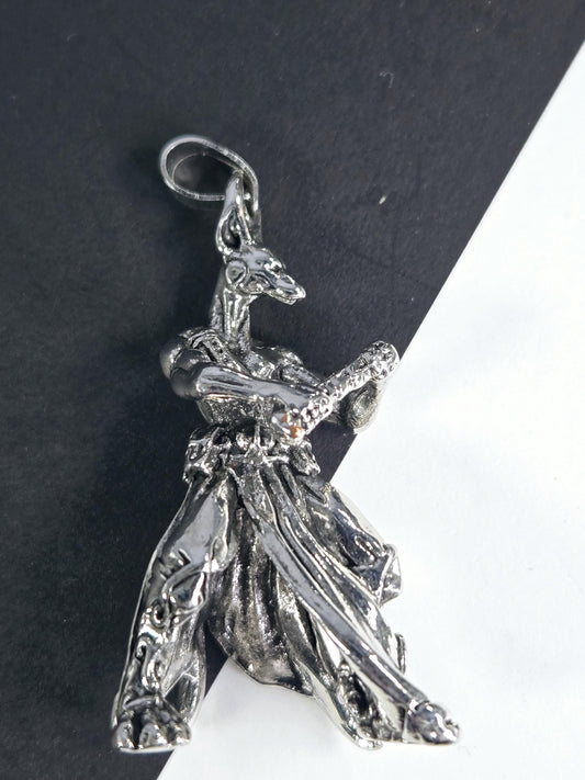 A silver-colored pendant or charm in the shape of a bird or a winged creature, resting on a black surface.