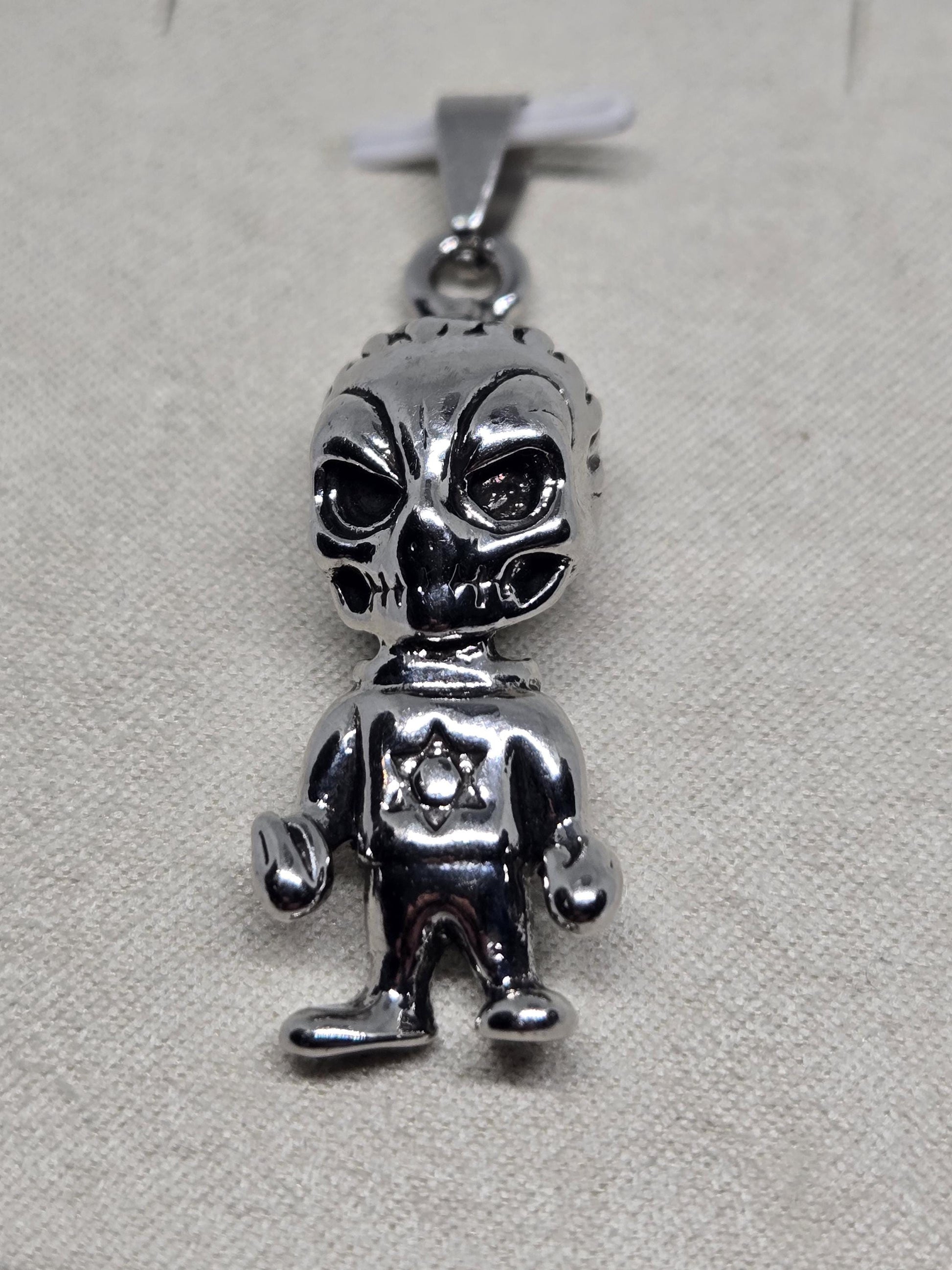 A silver-colored metal charm or bracelet with an alien or robot-like design.