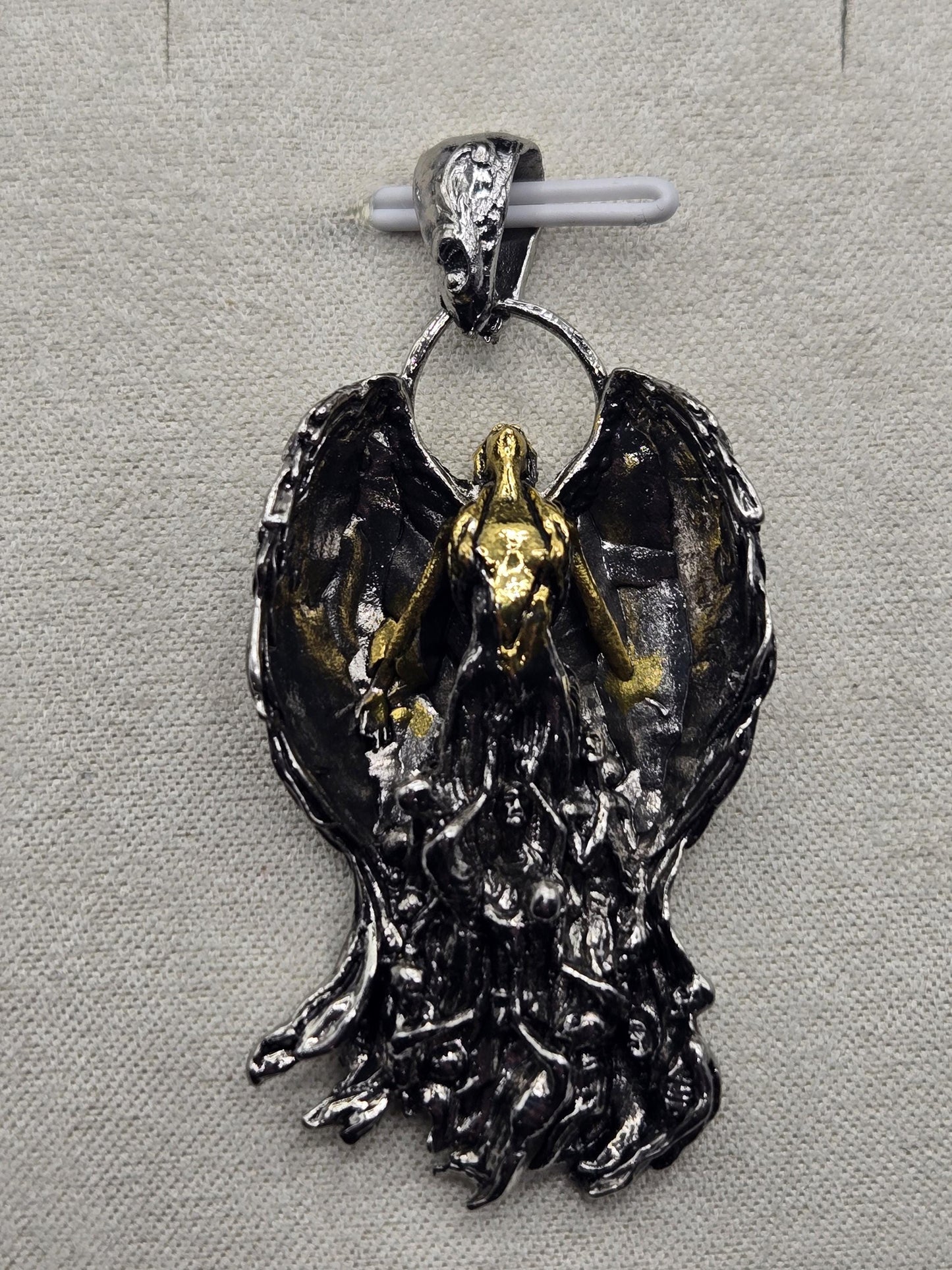 a pendant with a detailed design, including a metallic bird-like figure and a metallic chain.