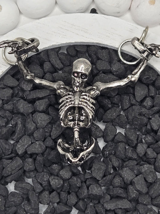A silver skeleton necklace with a pendant is displayed on a bed of small black stones.