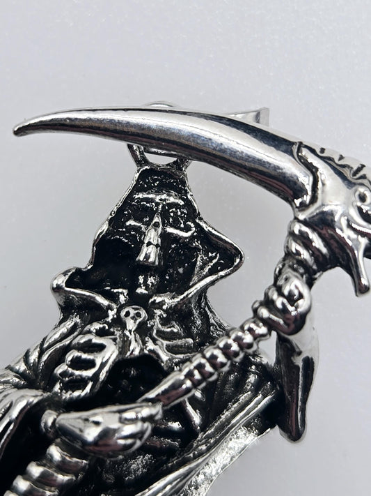 A close-up view of a silver metal sculpture depicting a skull-like figure with a curved, pointed horn-like object attached to it.