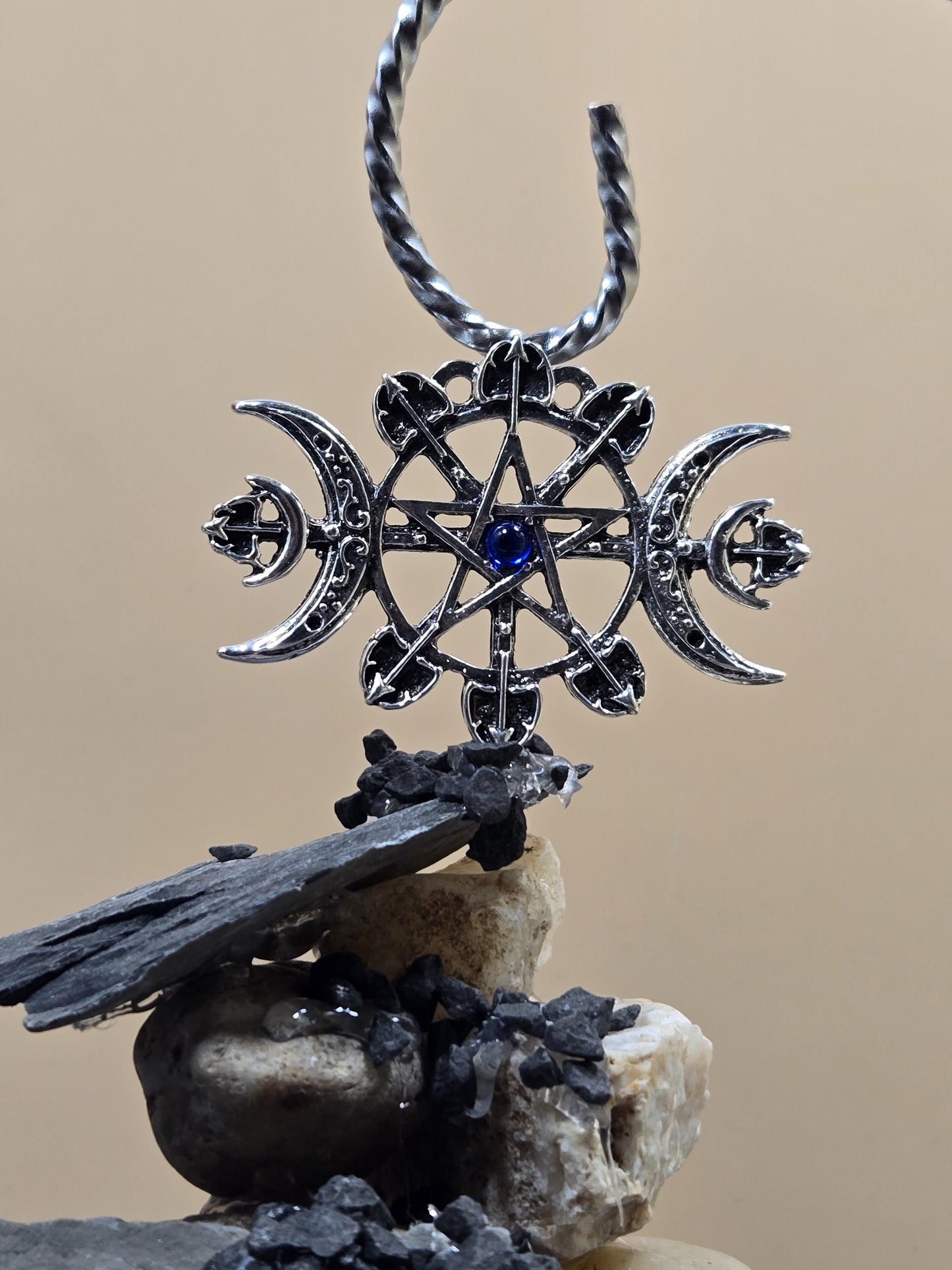 A silver pendant with a star design and a blue gemstone, hanging on a chain against a beige background.