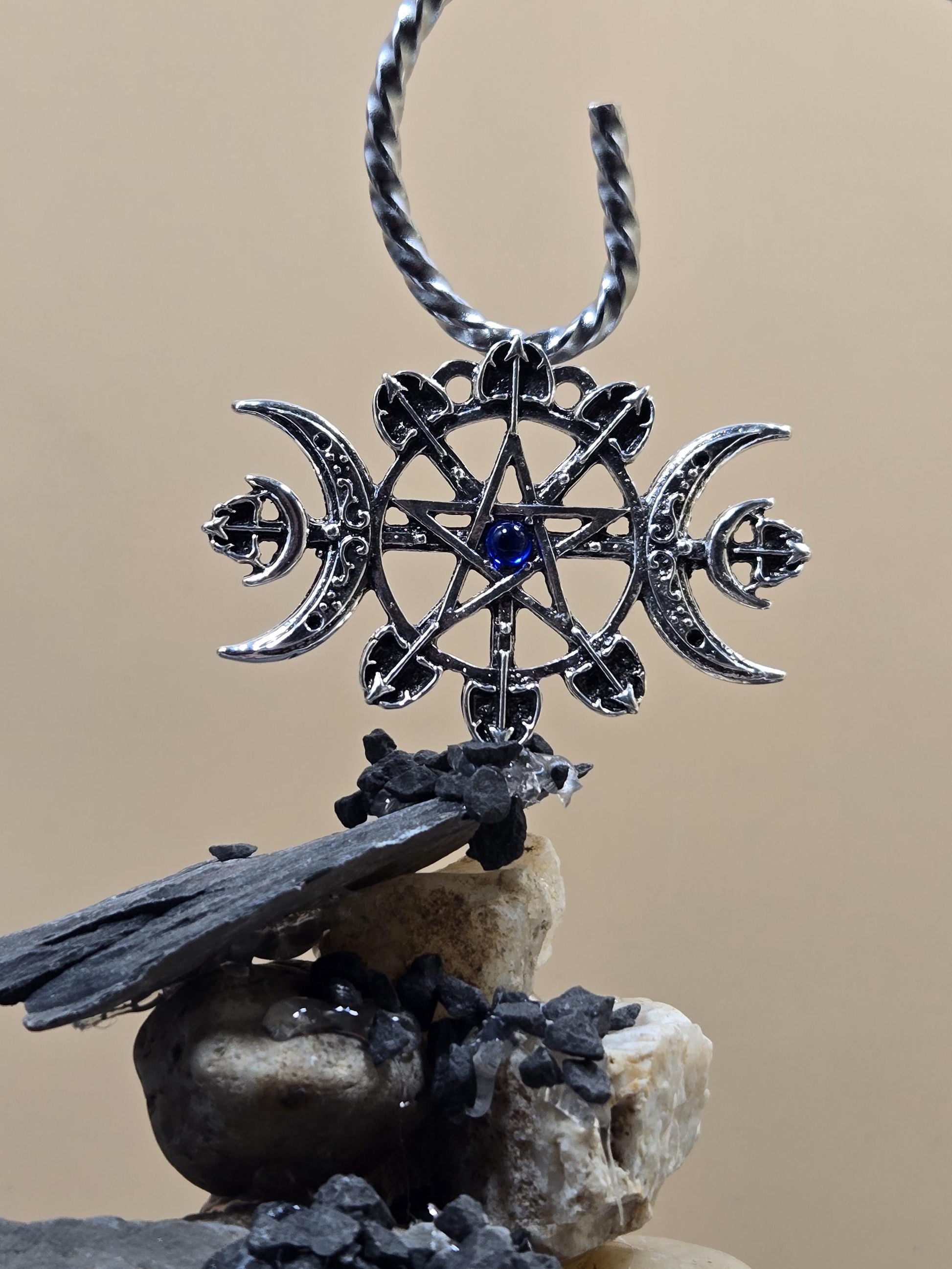 A silver pendant with a star design and a blue gemstone, hanging on a chain against a beige background.