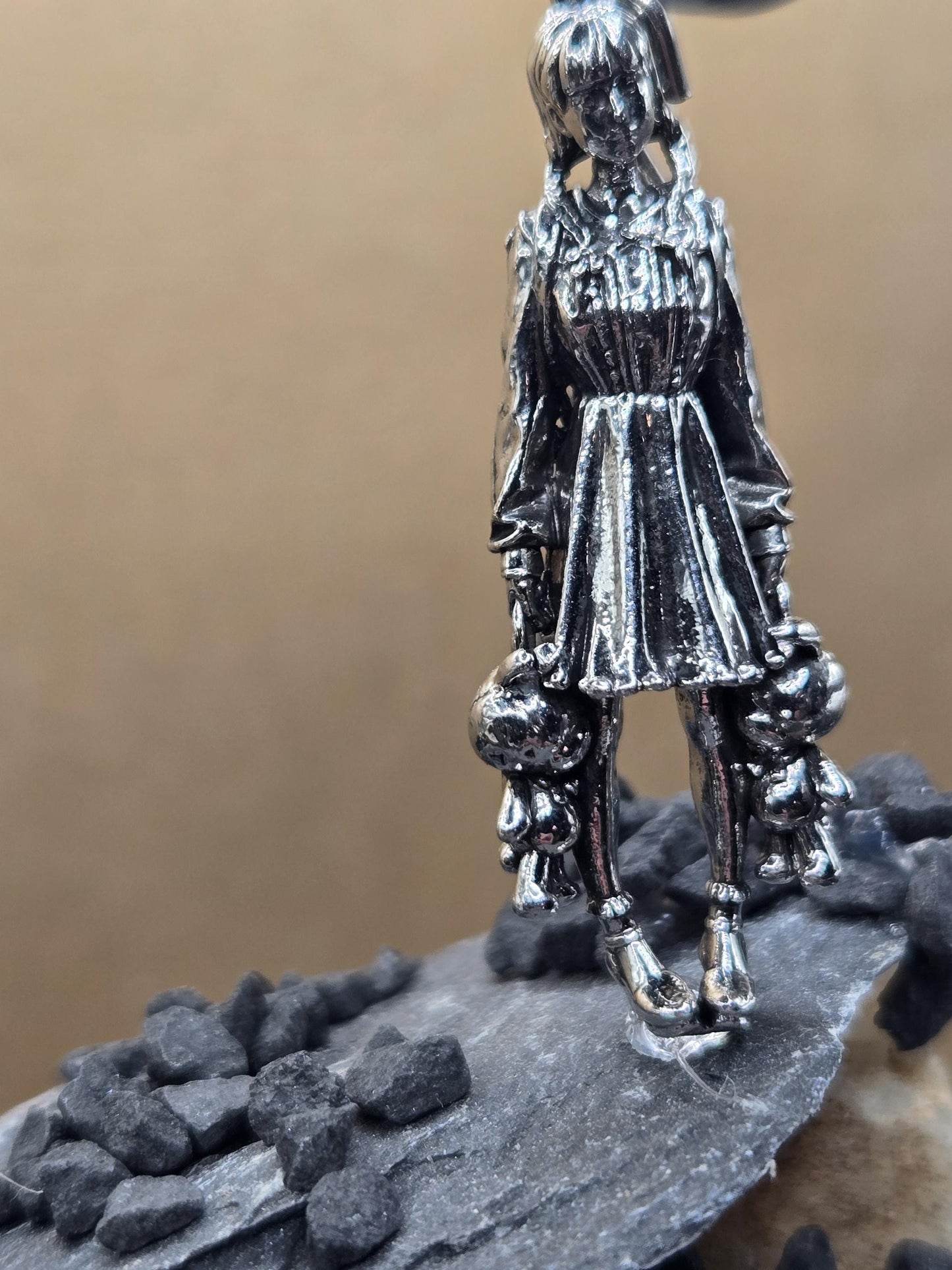 A close-up view of a silver-colored metal object, possibly a pendant or sculpture, with intricate details and a textured surface.