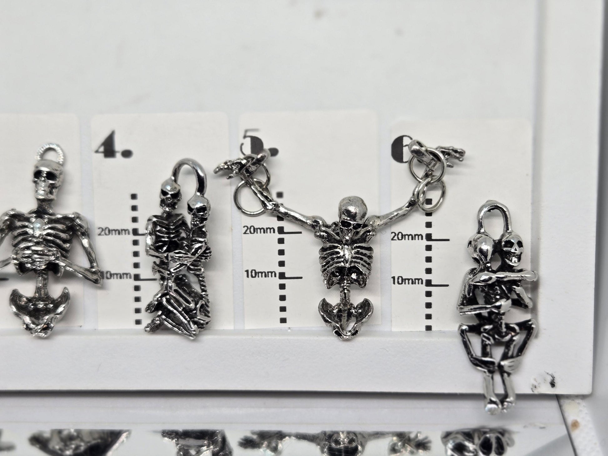 a collection of silver-colored metal charms, including skull-shaped pendants, arranged on a white surface.