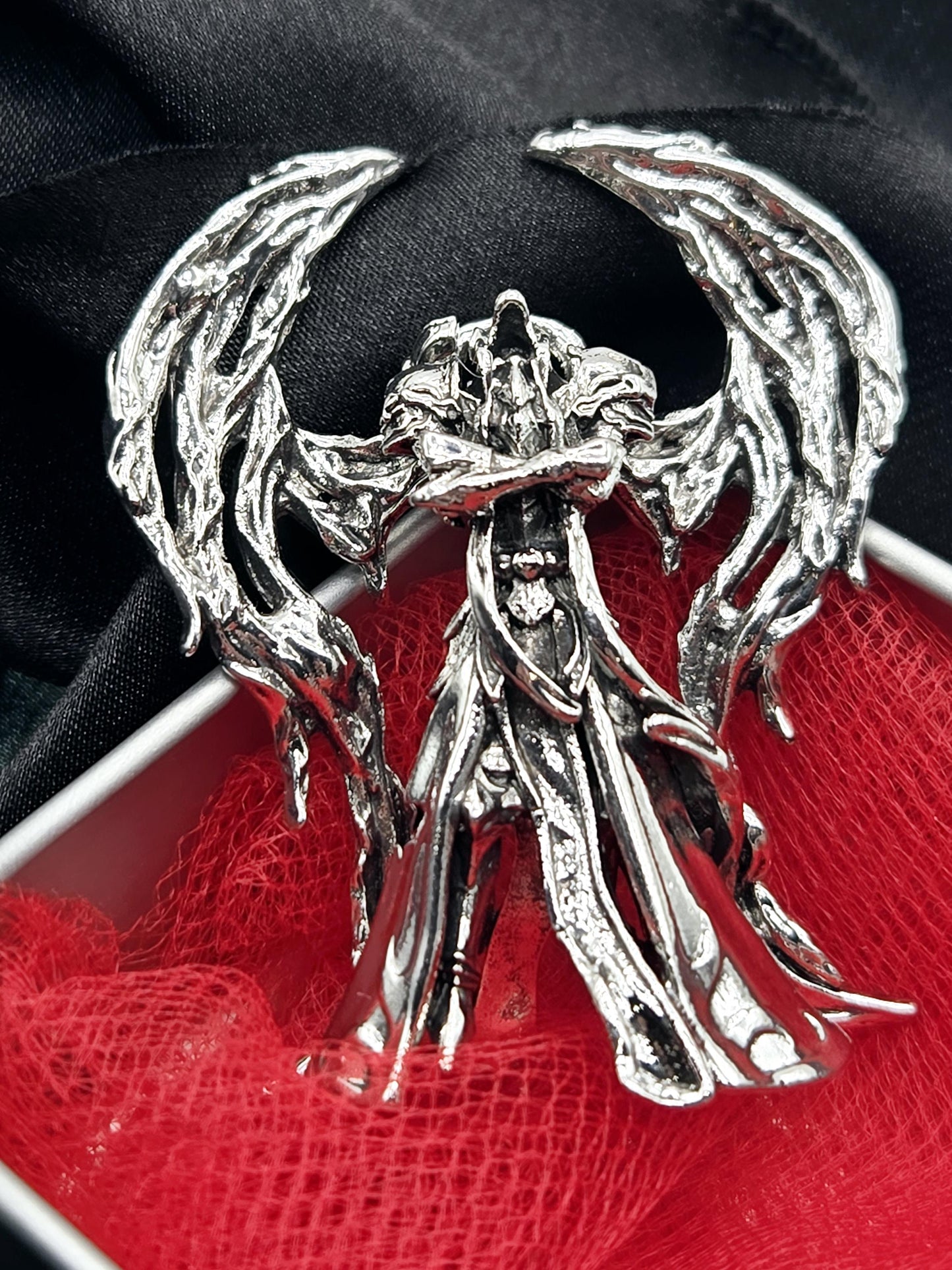 a silver brooch with an intricate, organic design, resting on a red fabric background.