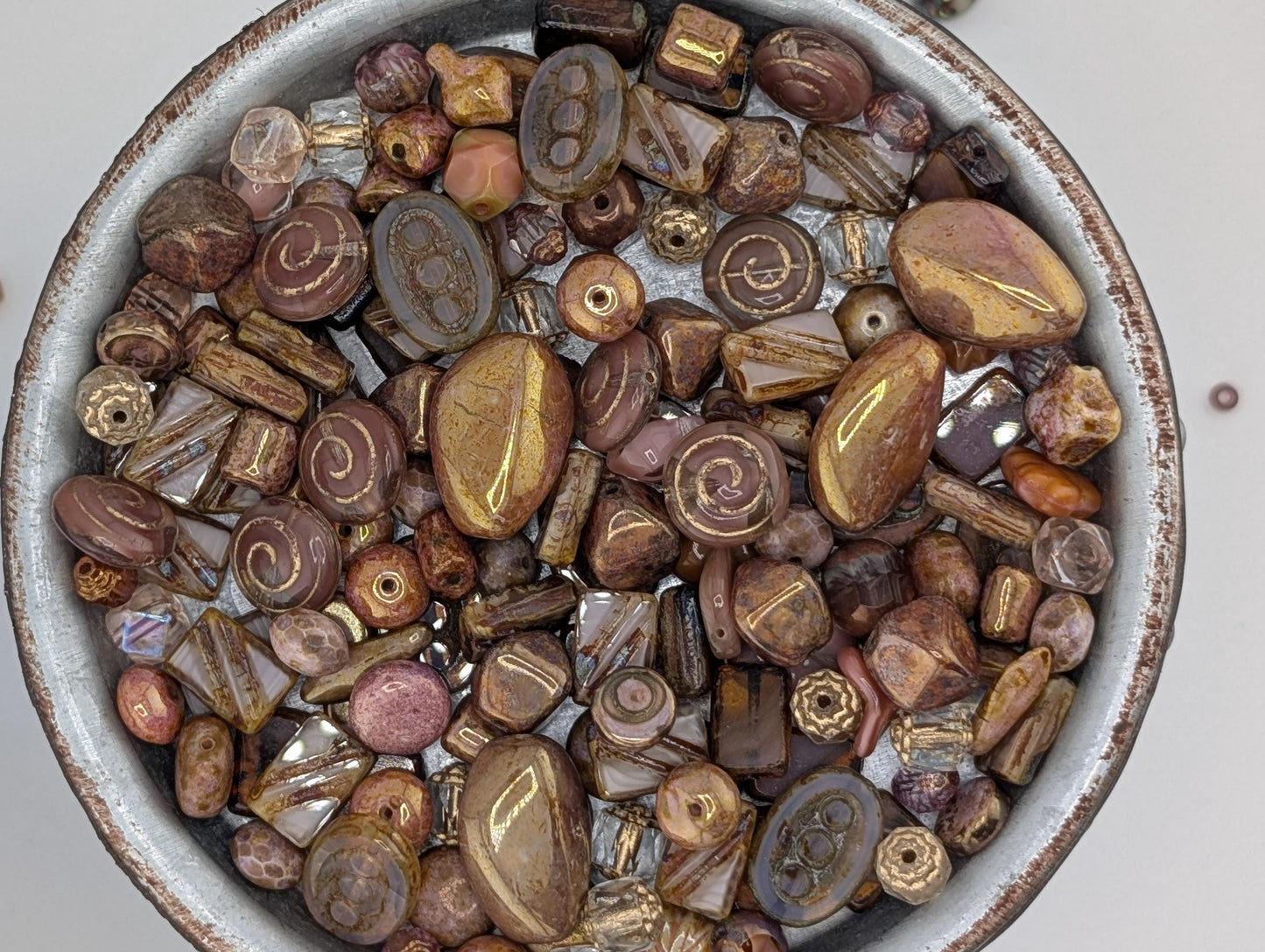 A bowl filled with various beads and stones, including gold, brown, and purple colors.