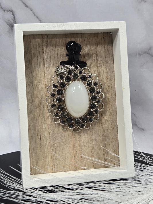 A white wooden box with a black clasp and a white oval-shaped brooch with black and silver accents, placed on a marble surface.