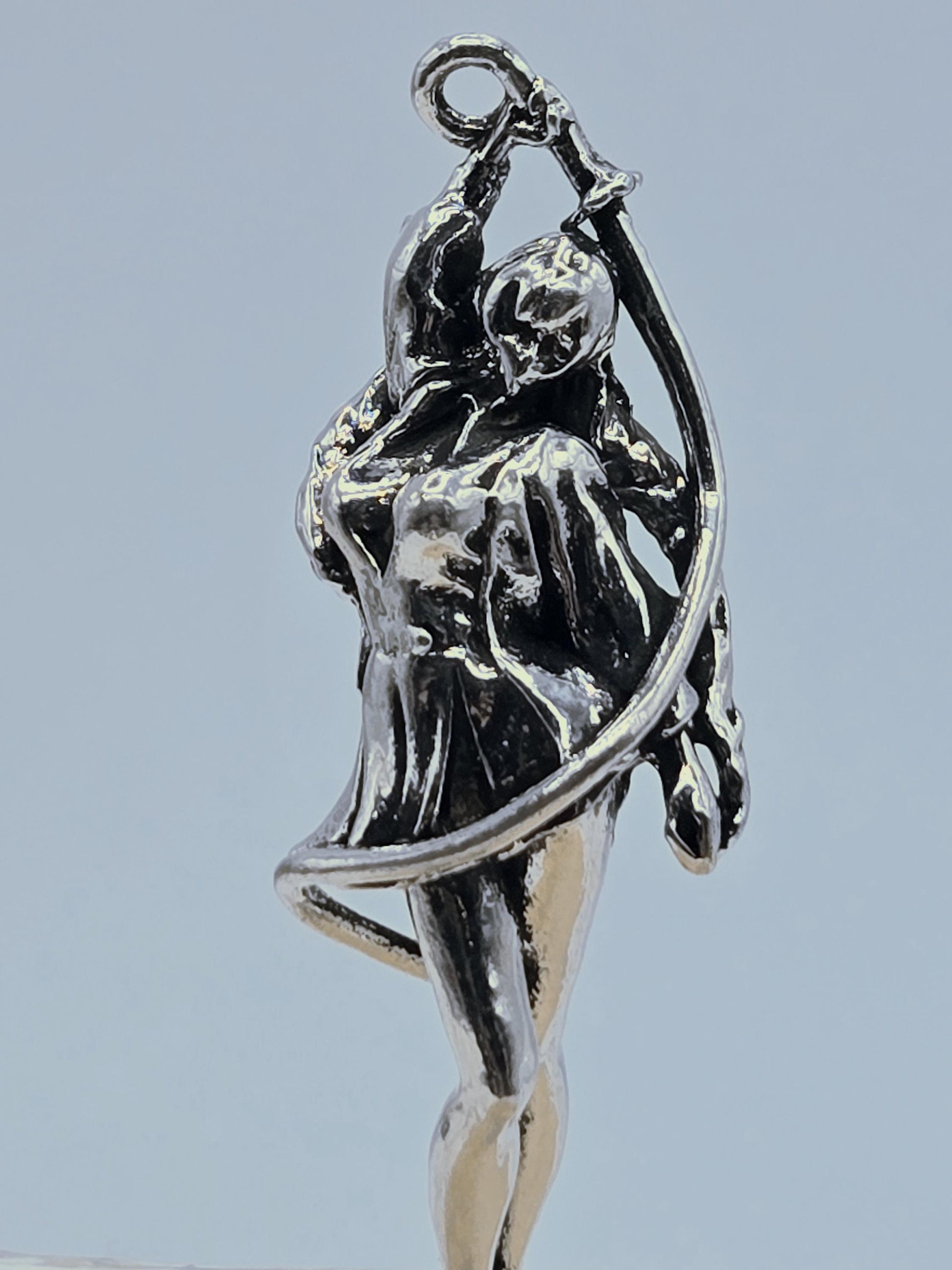 A close-up view of a silver-colored metal sculpture depicting a figure in a dynamic pose, with a curved arm and a flowing, abstract design.