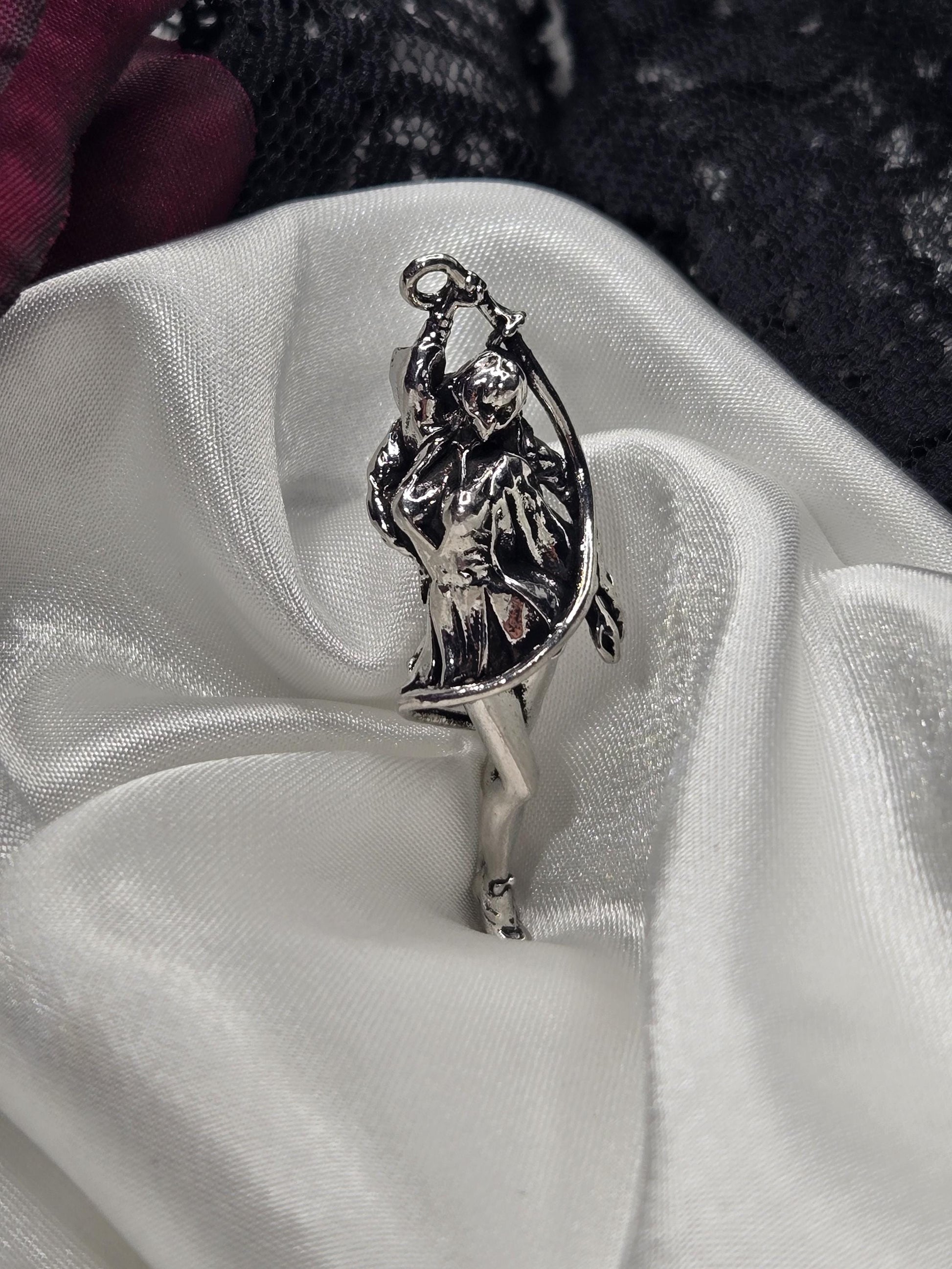 A silver-colored metal charm or pendant is resting on a white fabric surface.