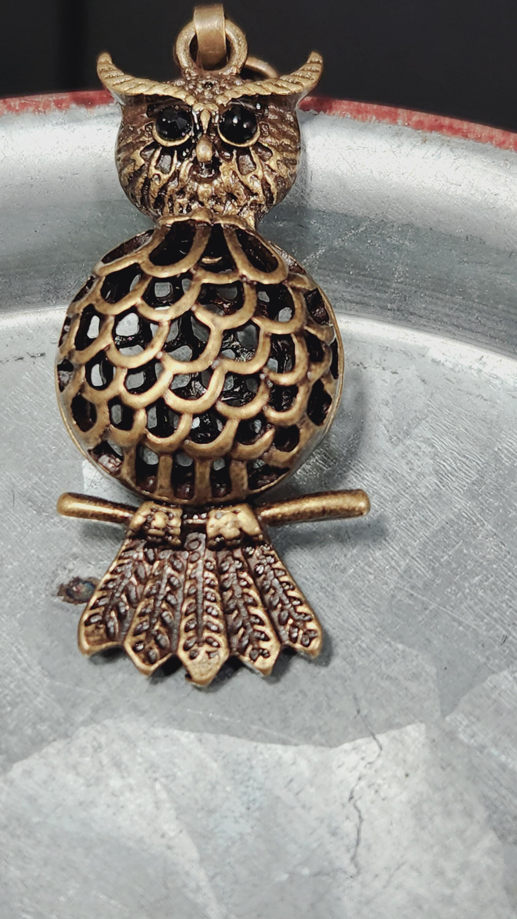 A close-up image of a decorative metal owl pendant with a detailed, intricate design.