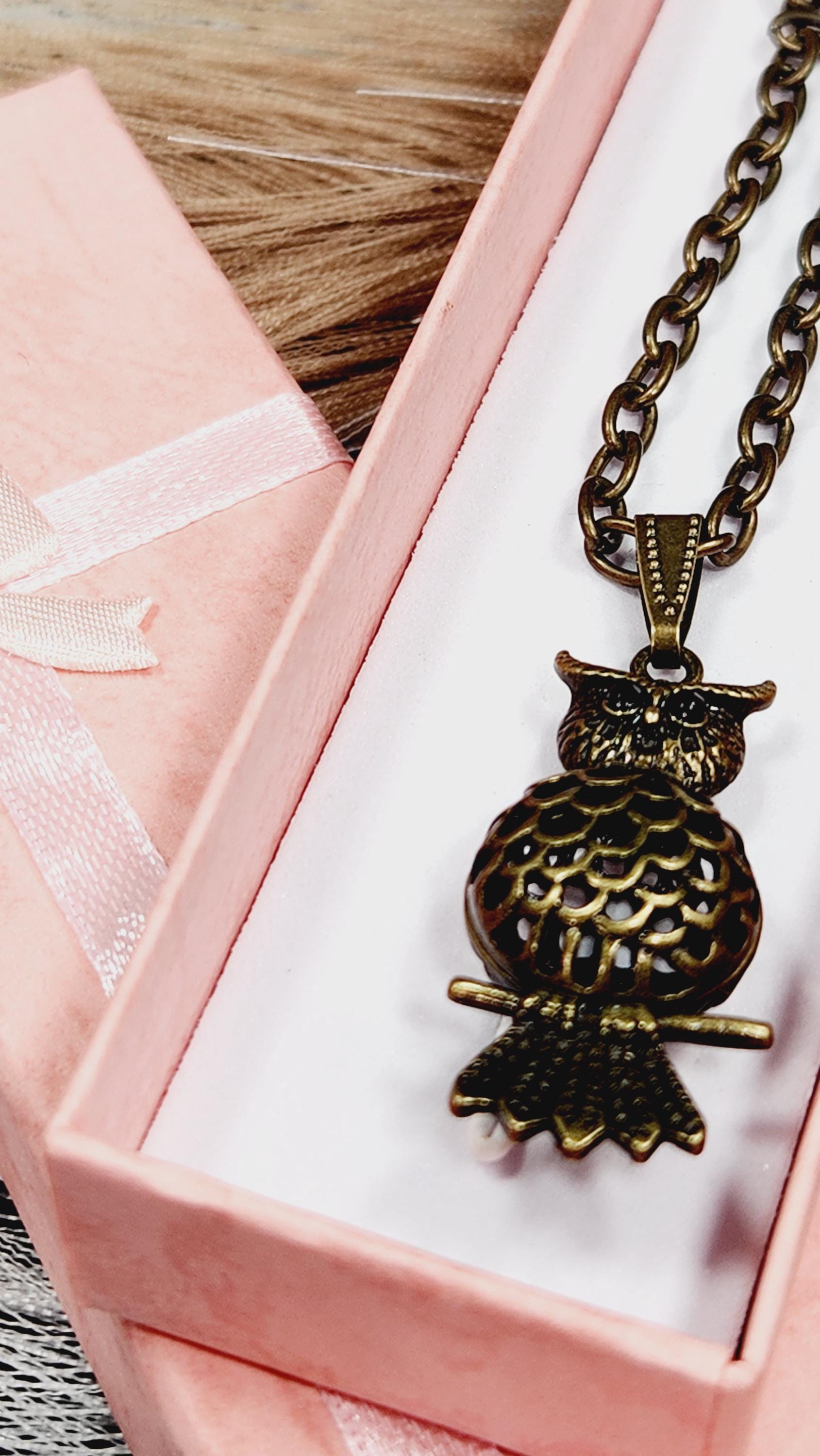 A close-up view of a decorative pendant necklace with a metallic design, displayed in a pink box with a white ribbon.