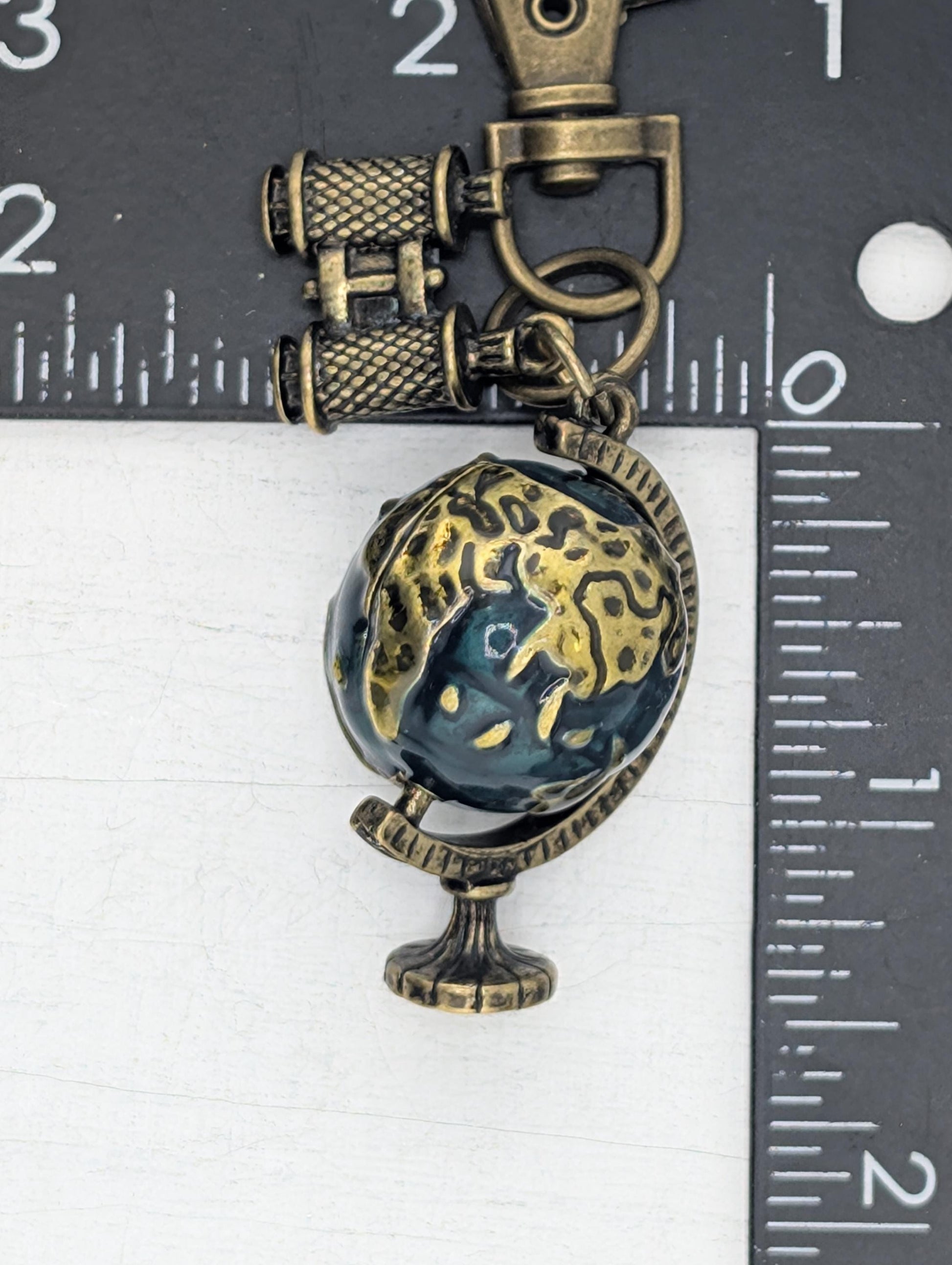 A decorative metal globe charm with a blue and gold design, attached to a keychain.
