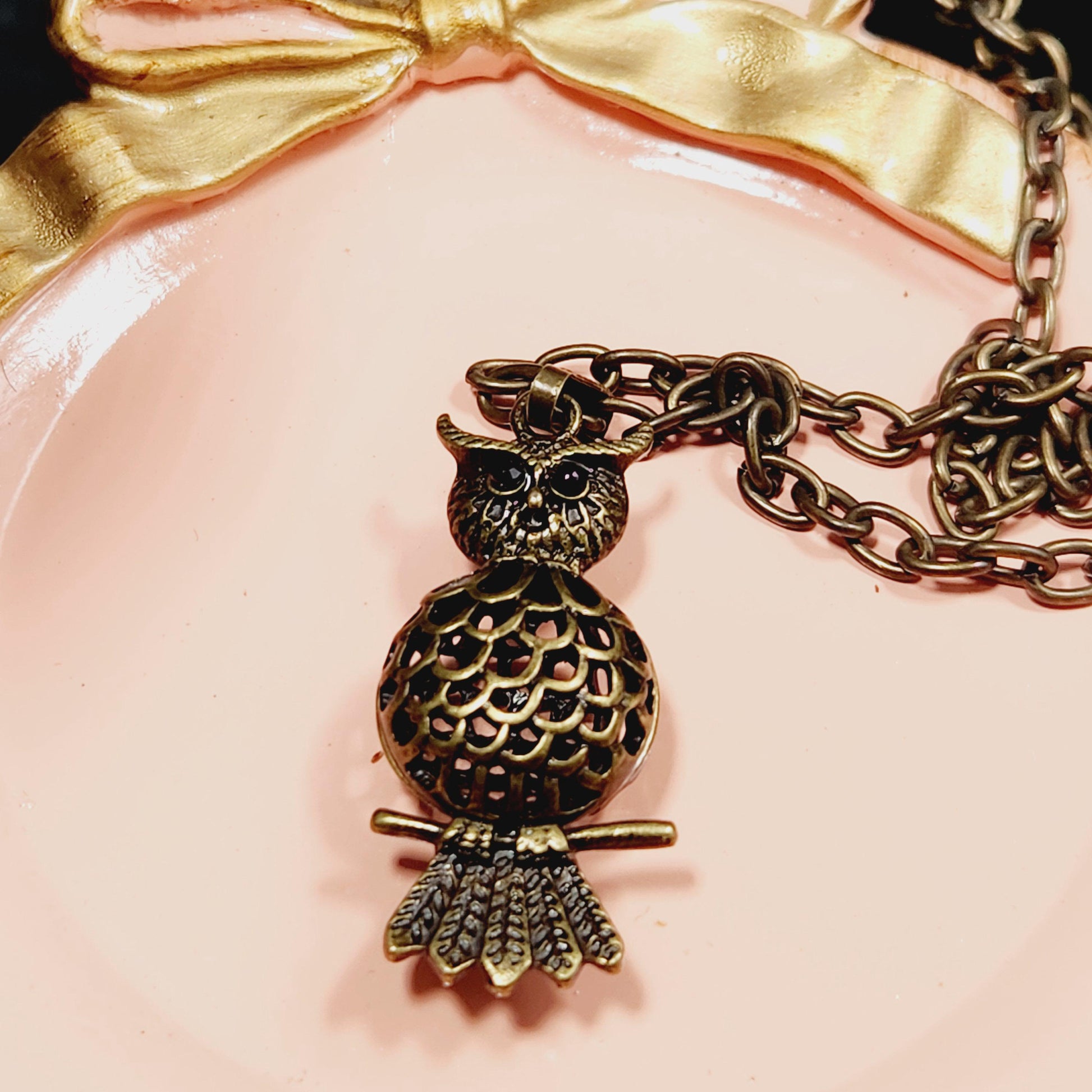 A close-up image of a decorative necklace with a pendant in the shape of a bird, resting on a pink surface.