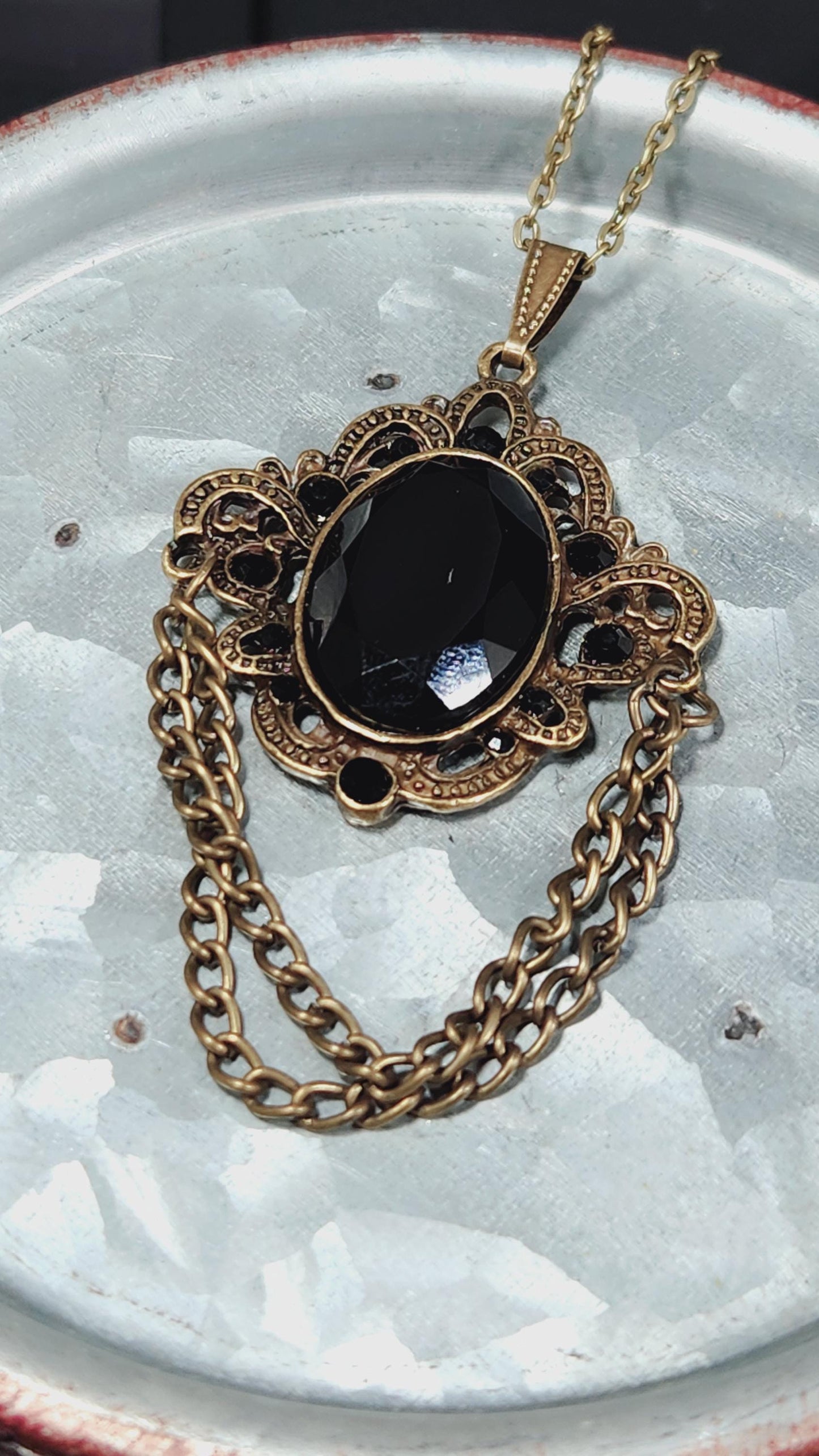 A black gemstone pendant with an ornate gold chain is displayed on a white plate.