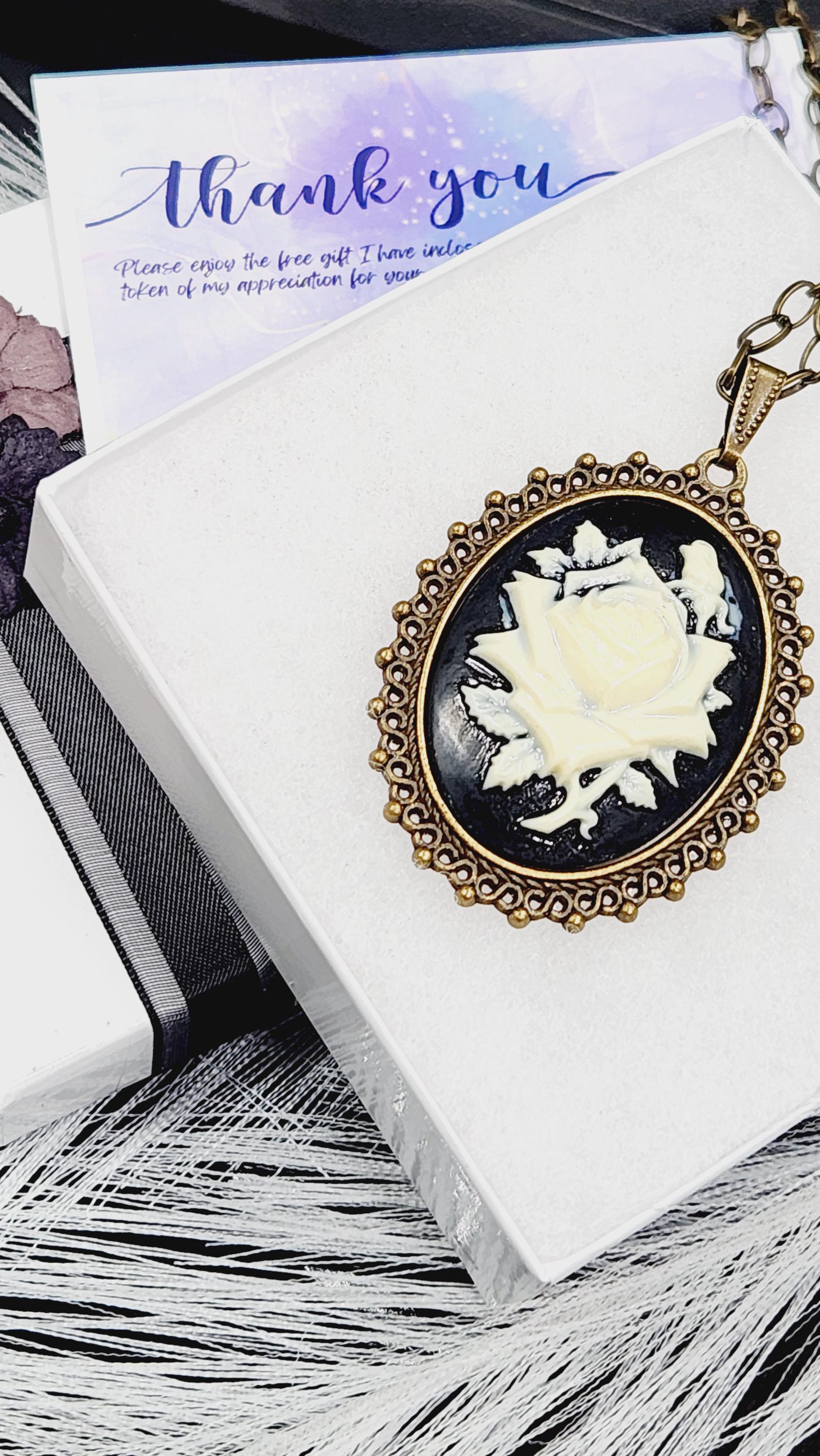 A pendant with a white rose design is displayed on a white surface, accompanied by a purple card with a &quot;Thank you&quot; message.