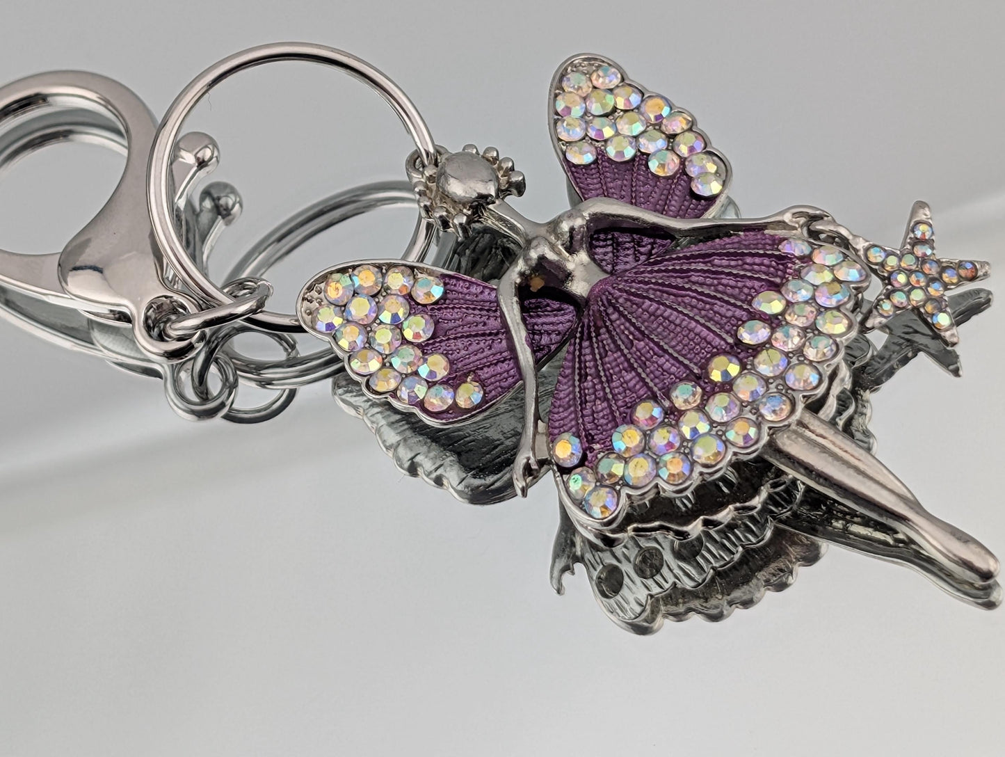 A keychain with a purple fairy design, featuring a star and a butterfly motif, adorned with sparkling rhinestones.