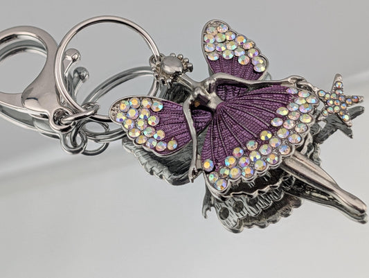 A keychain with a purple fairy design, featuring a star and a butterfly motif, adorned with sparkling rhinestones.