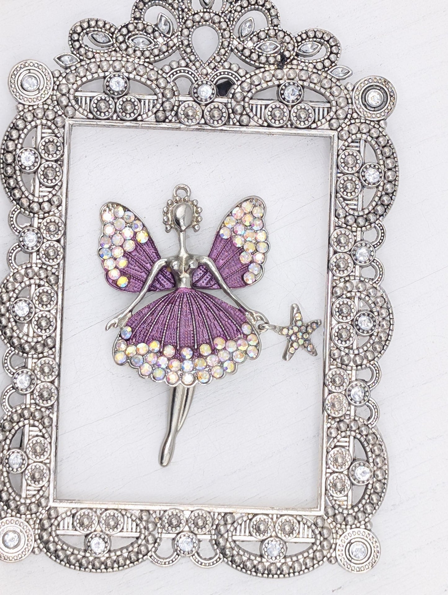 A silver-colored frame with a decorative border, containing a purple butterfly-shaped pendant adorned with rhinestones and a star-shaped charm.
