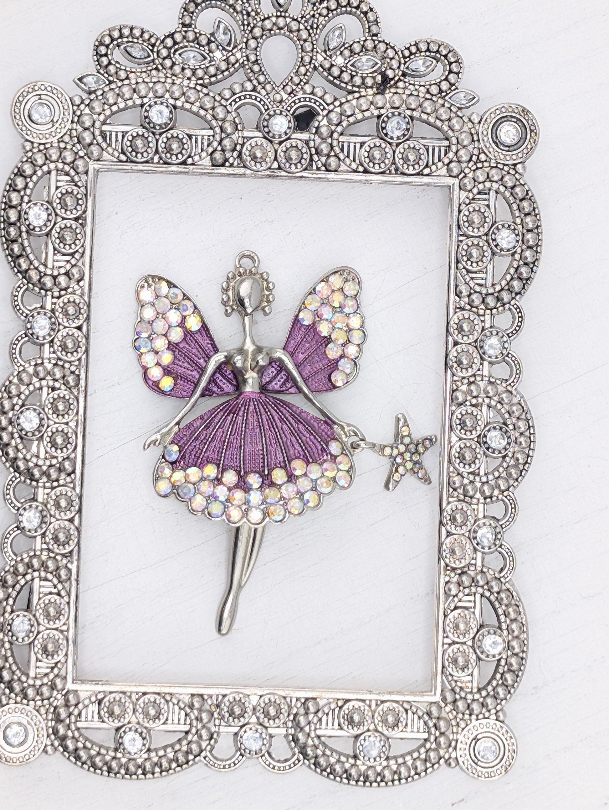 A silver-colored frame with a decorative border, containing a purple butterfly-shaped pendant adorned with rhinestones and a star-shaped charm.