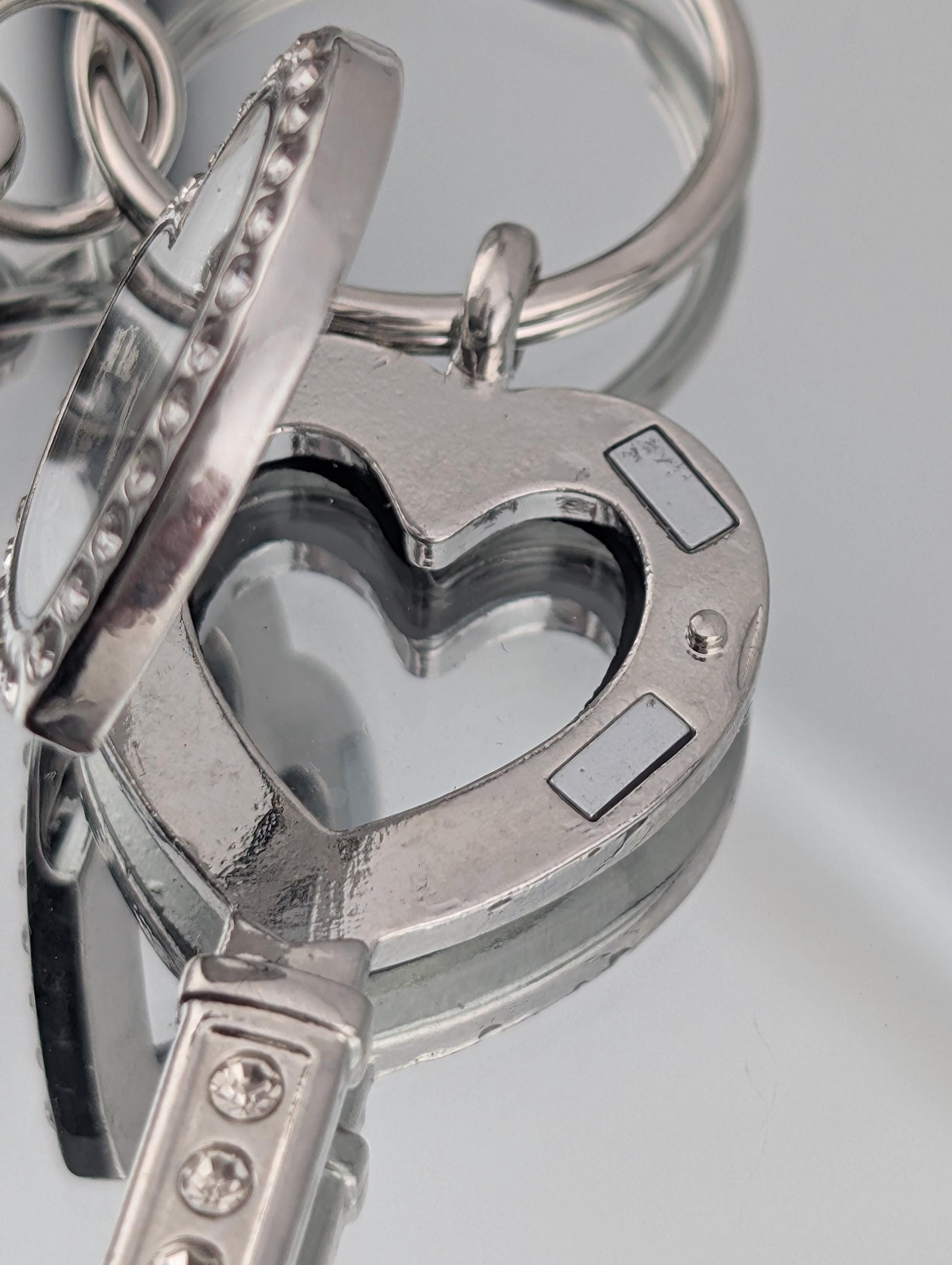 A close-up view of a heart-shaped keychain with a reflective surface, featuring a keyring and a key attached to it.