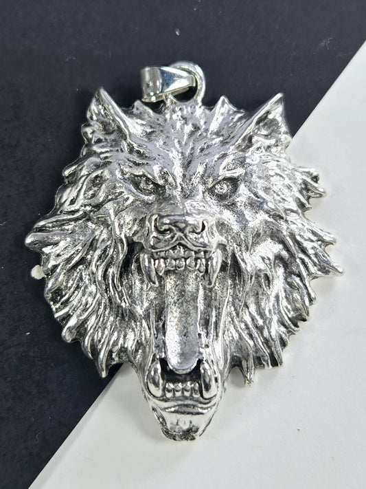 A silver-colored metal pendant in the shape of a fierce-looking animal head, possibly a wolf or a lion, with sharp teeth and an intense expression.