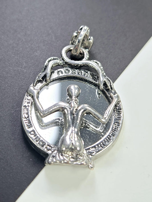 A silver-colored pendant or charm with an intricate design, featuring a figure or symbol within a circular frame.