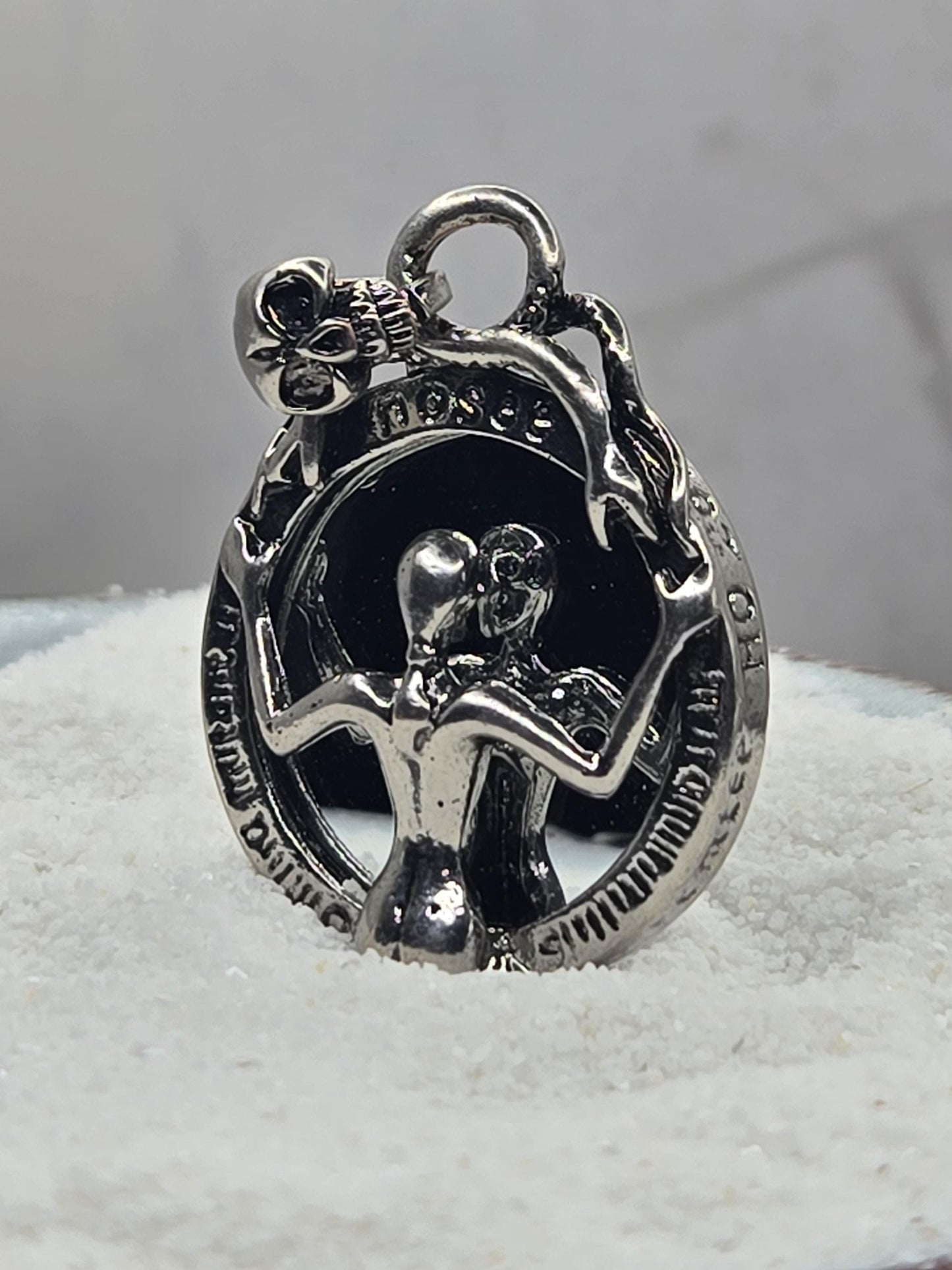 A silver-colored metal charm or pendant with an intricate design, including a skull and crossbones motif, and a small bell-like element.