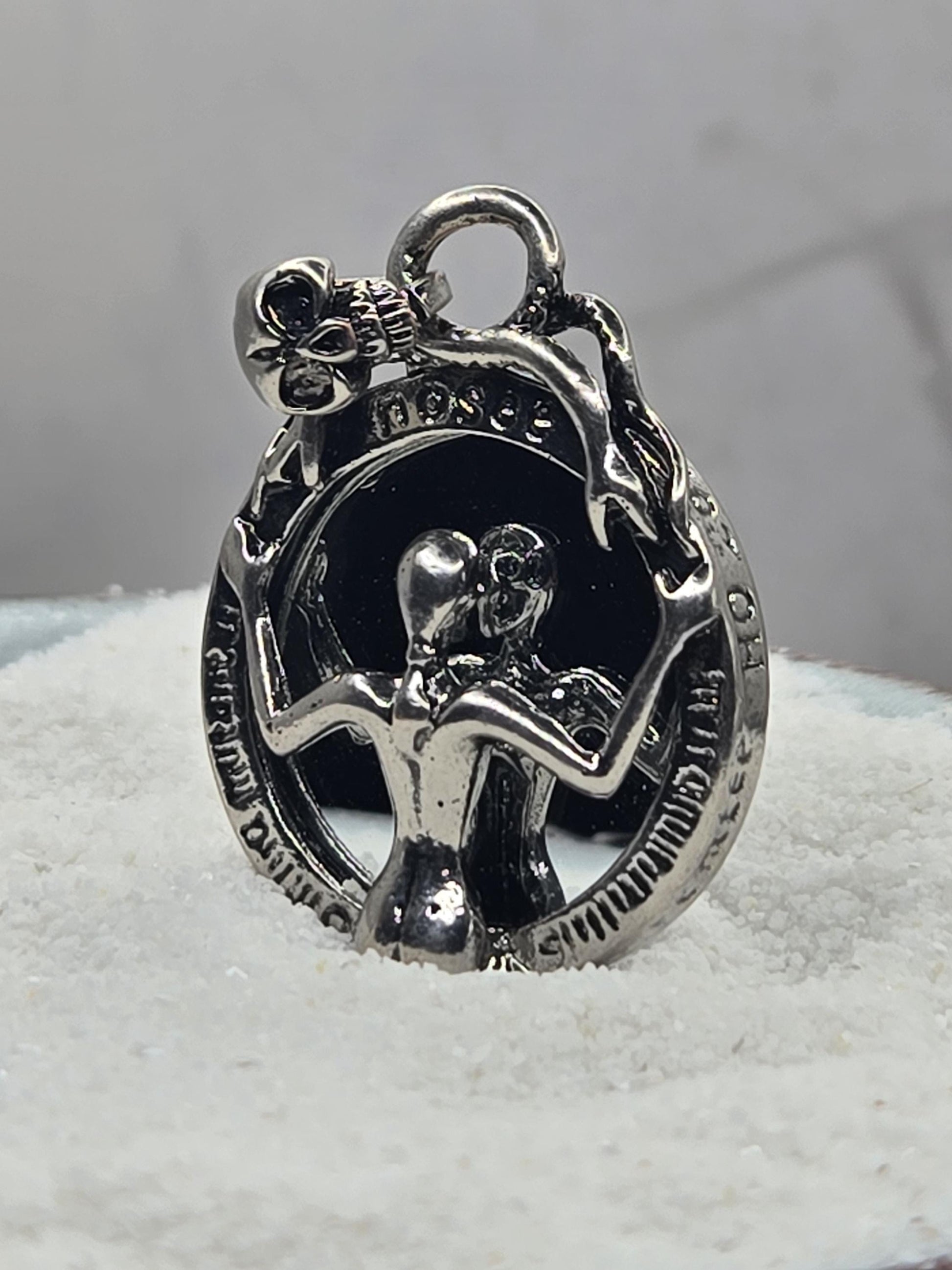 A silver-colored metal charm or pendant with an intricate design, including a skull and crossbones motif, and a small bell-like element.