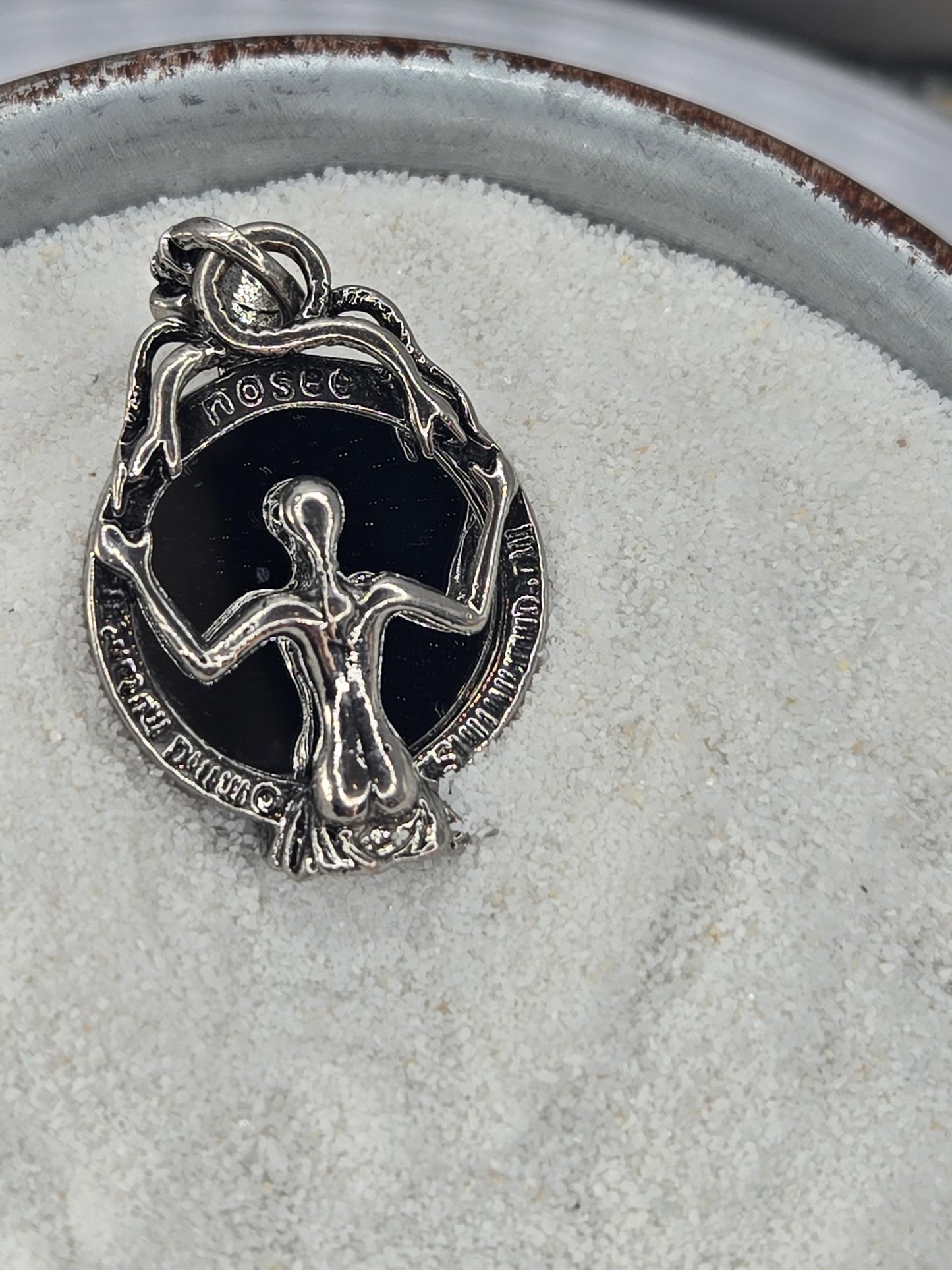 A silver-colored pendant or charm with an intricate design, resting on a white surface.