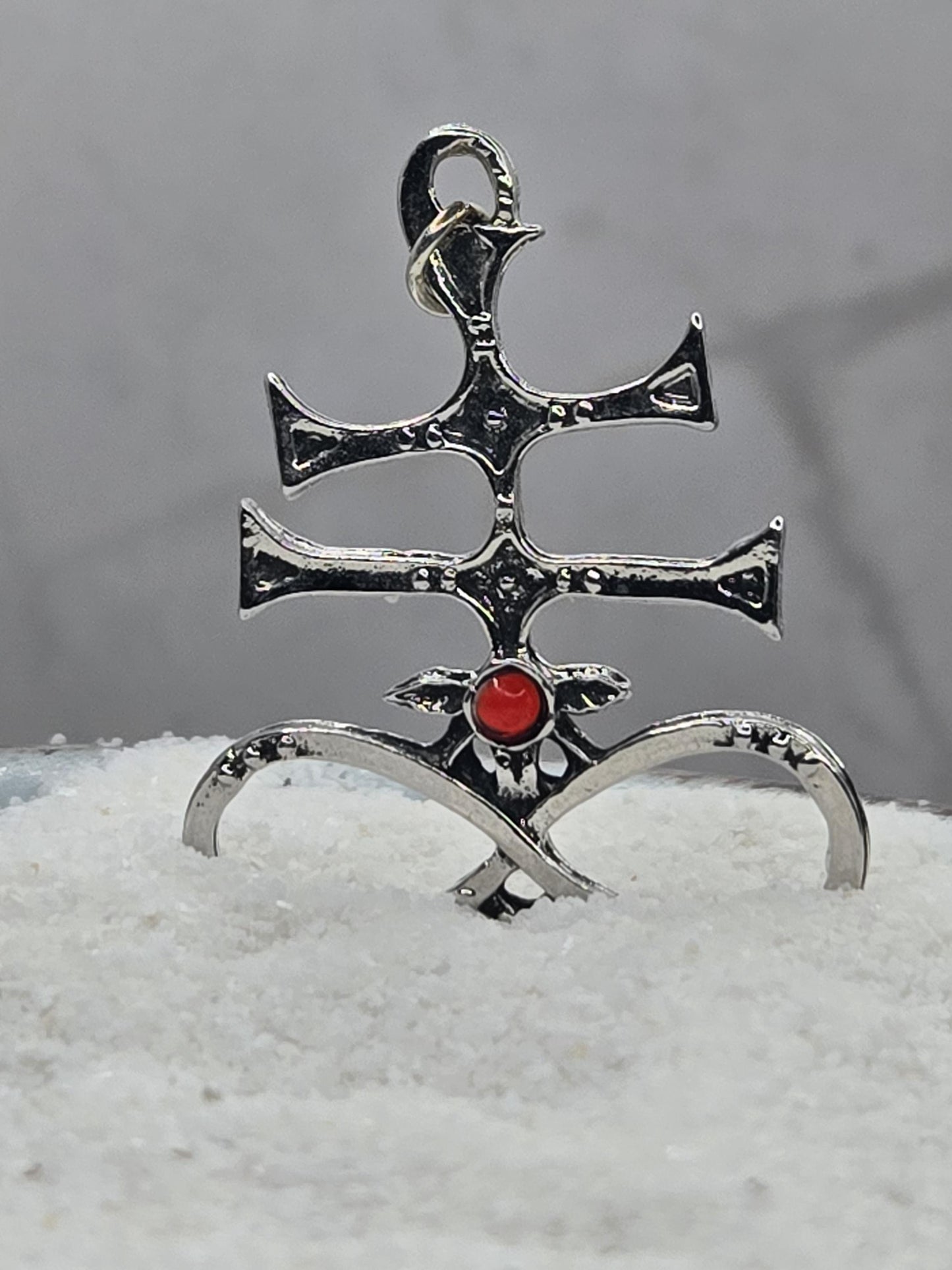 A silver-colored metal pendant with a red gemstone, featuring an intricate design.