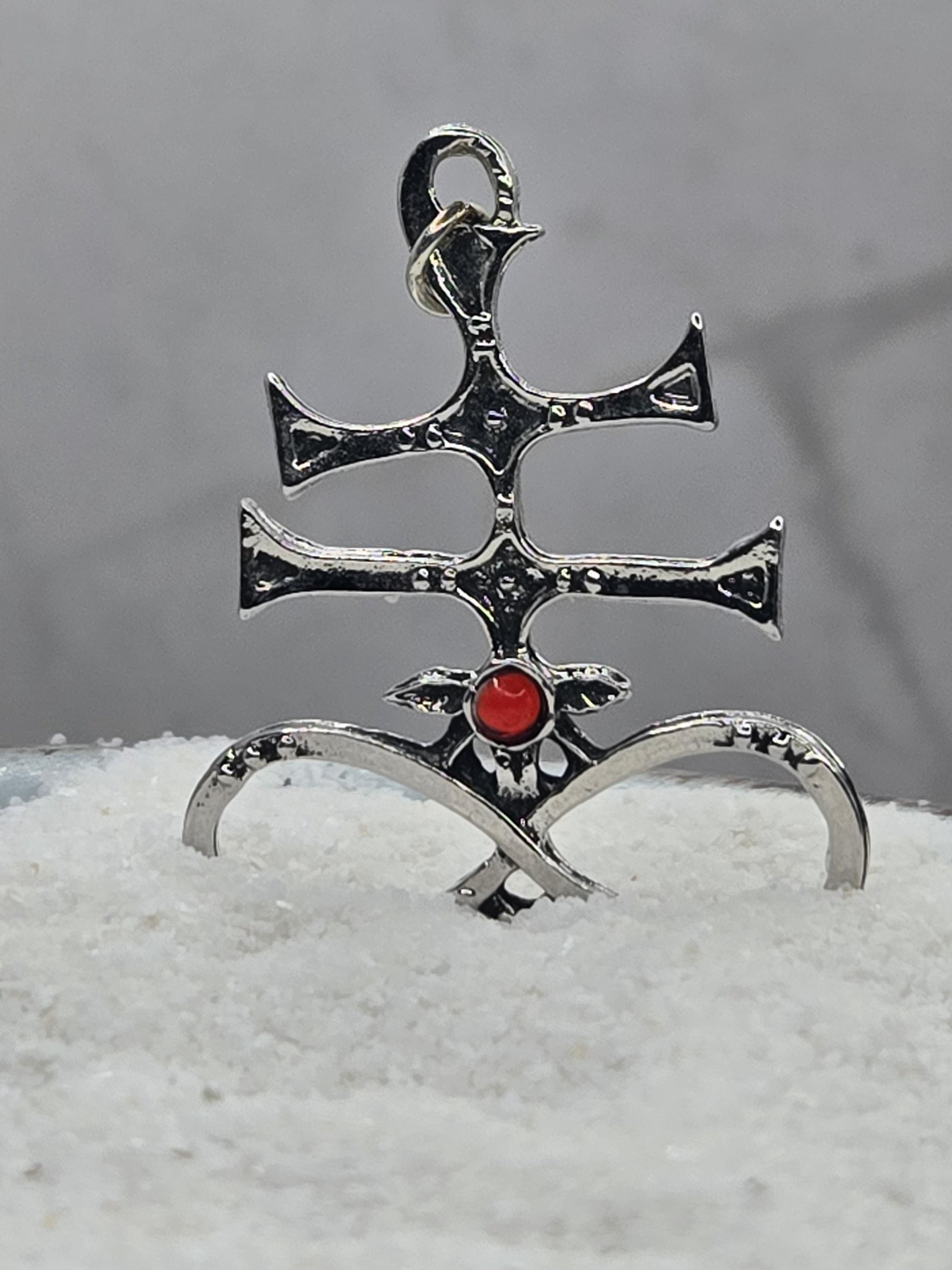 A silver-colored metal pendant with a red gemstone, featuring an intricate design.