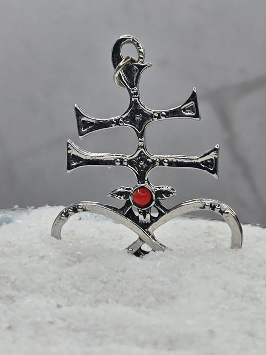 A silver-colored metal pendant with a red gemstone, featuring an intricate design.