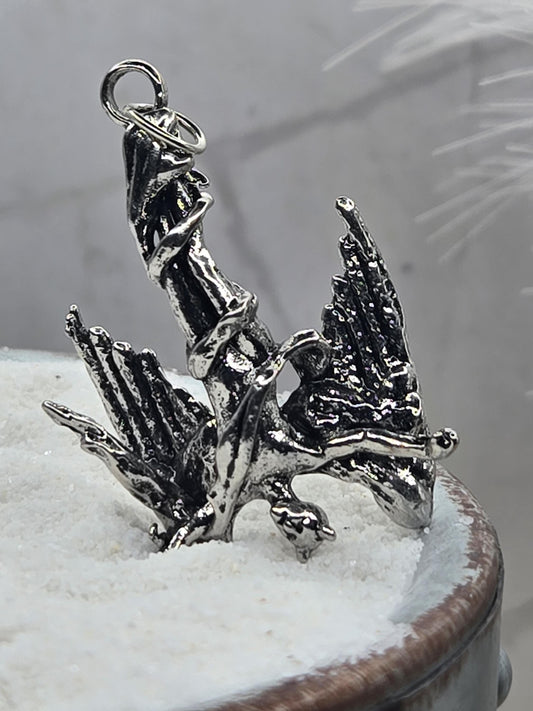 A close-up image of a silver-colored metal sculpture or ornament, possibly a pendant or charm, attached to a surface.
