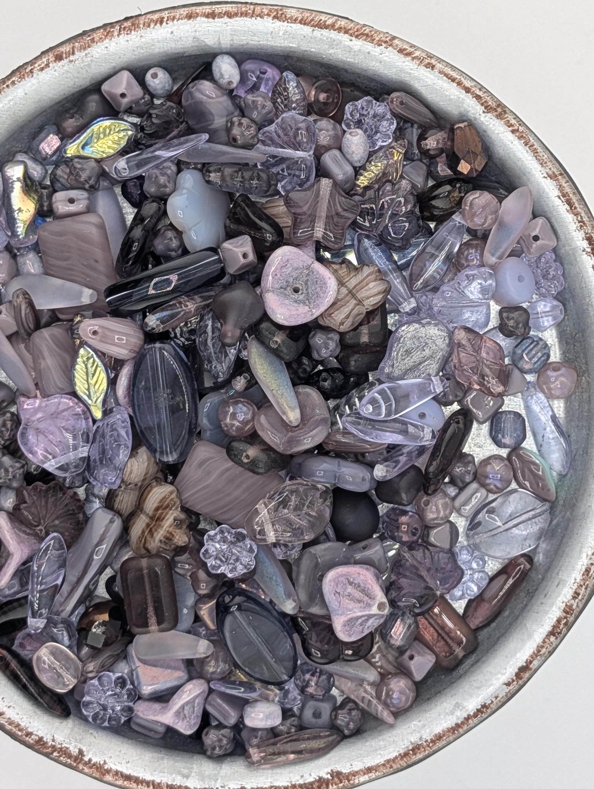 a bowl filled with various glass beads in shades of purple and gray, including clear and multicolored beads.