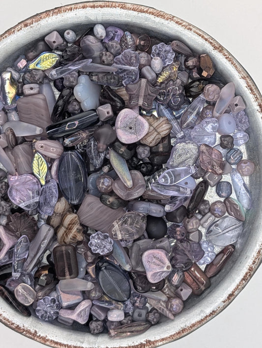 a bowl filled with various glass beads in shades of purple and gray, including clear and multicolored beads.