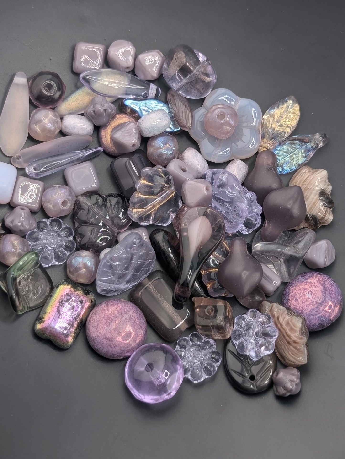 a variety of colorful glass beads and stones, including clear, purple, and multicolored pieces, scattered on a dark surface.