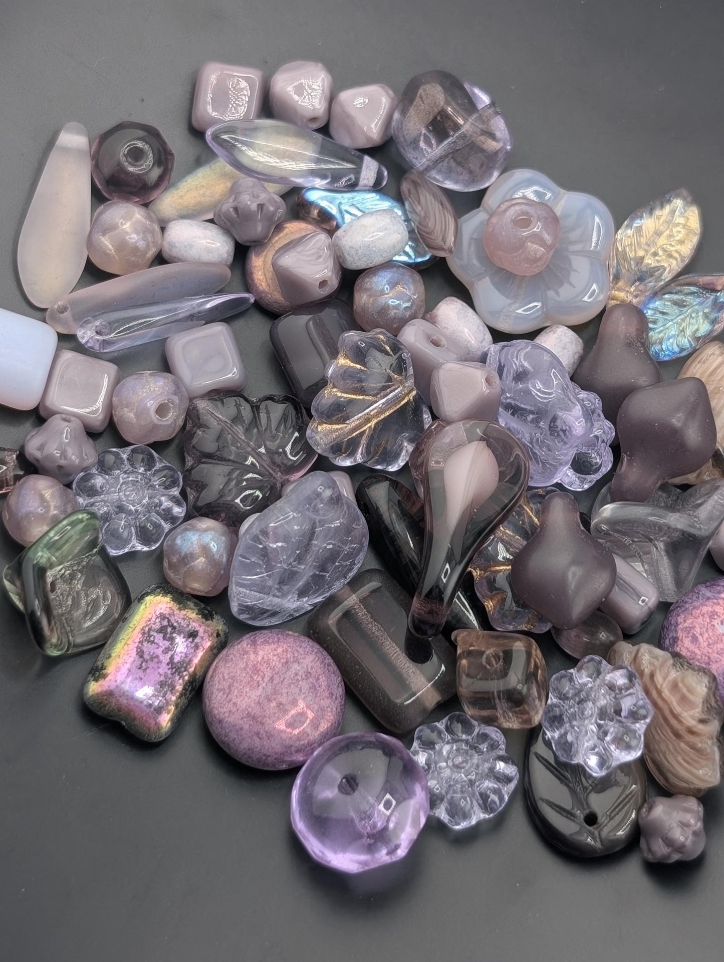 a variety of colorful glass beads and stones, including clear, purple, and multicolored pieces, arranged on a dark surface.