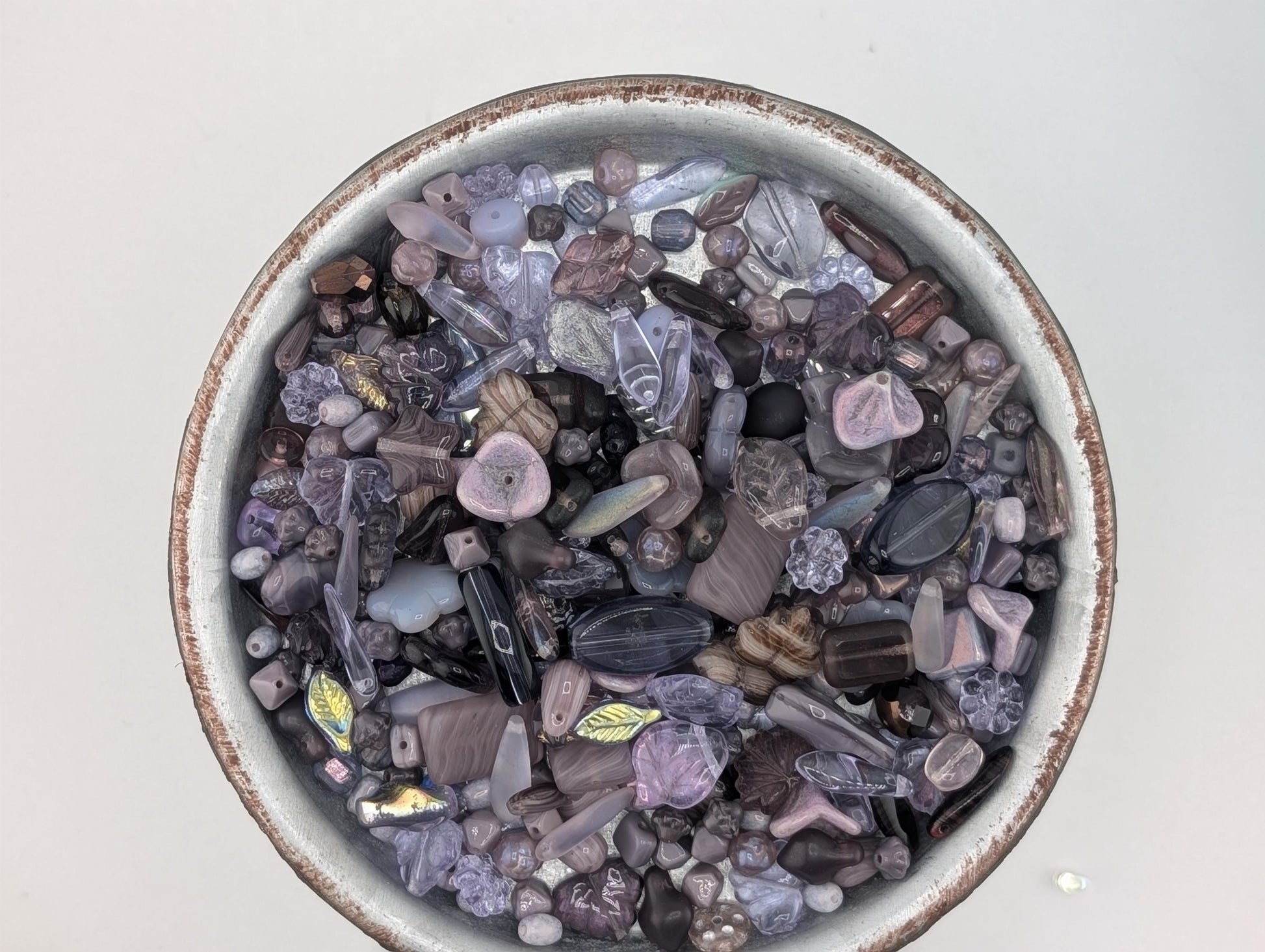 A bowl filled with various colorful beads, including purple, black, and multicolored stones, is shown in the image.