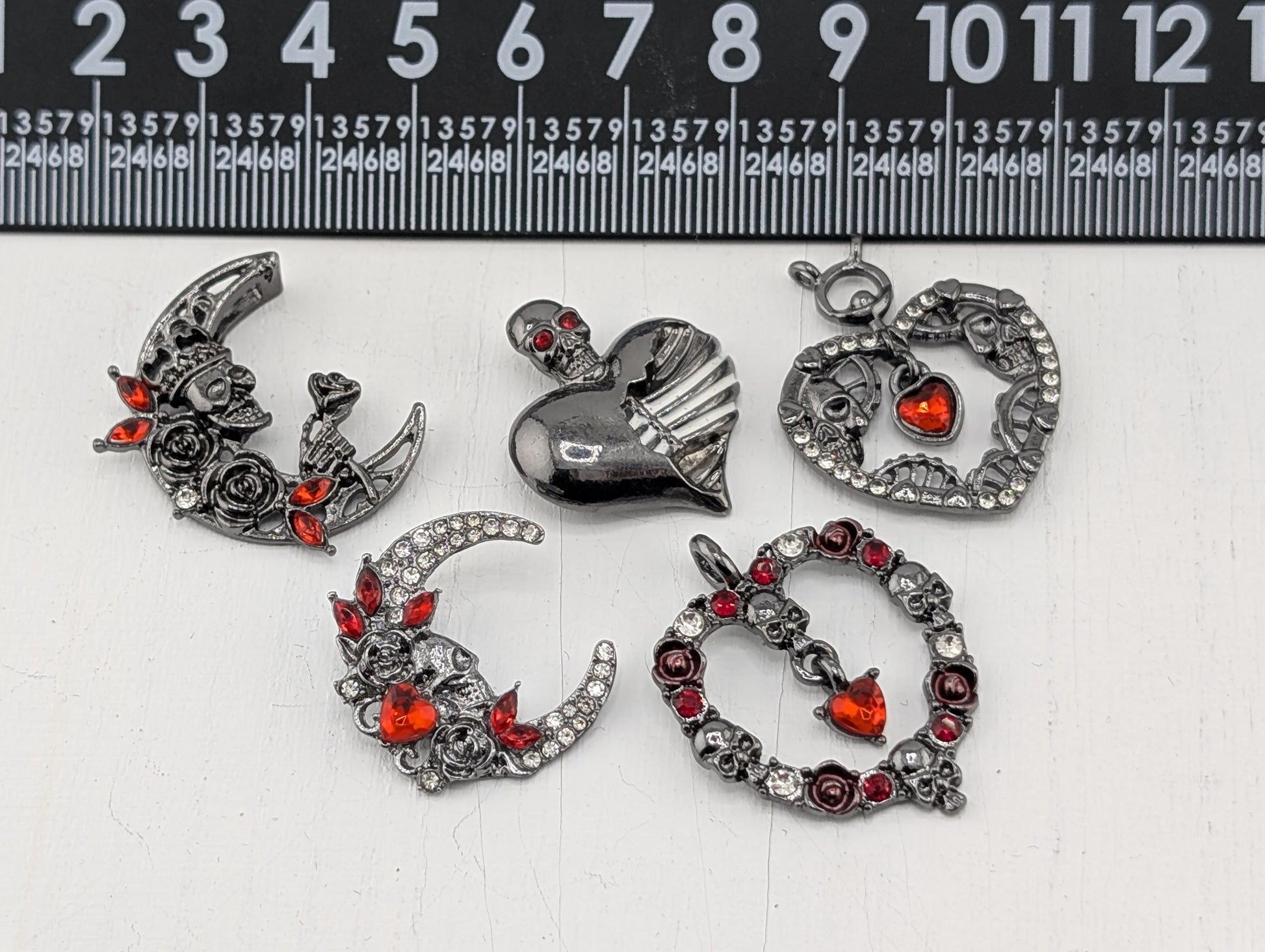 a collection of ornate, metallic jewelry pieces, including brooches, pendants, and charms, adorned with red gemstones and intricate designs.