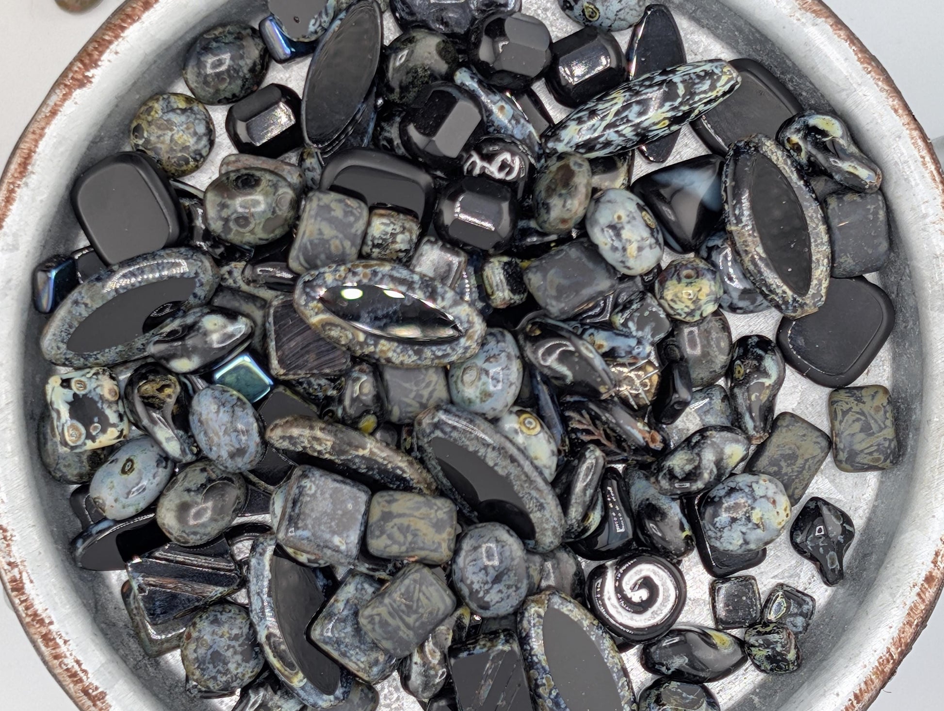 A bowl filled with various black and gray stones, including crystals and gemstones, arranged in a visually appealing manner.