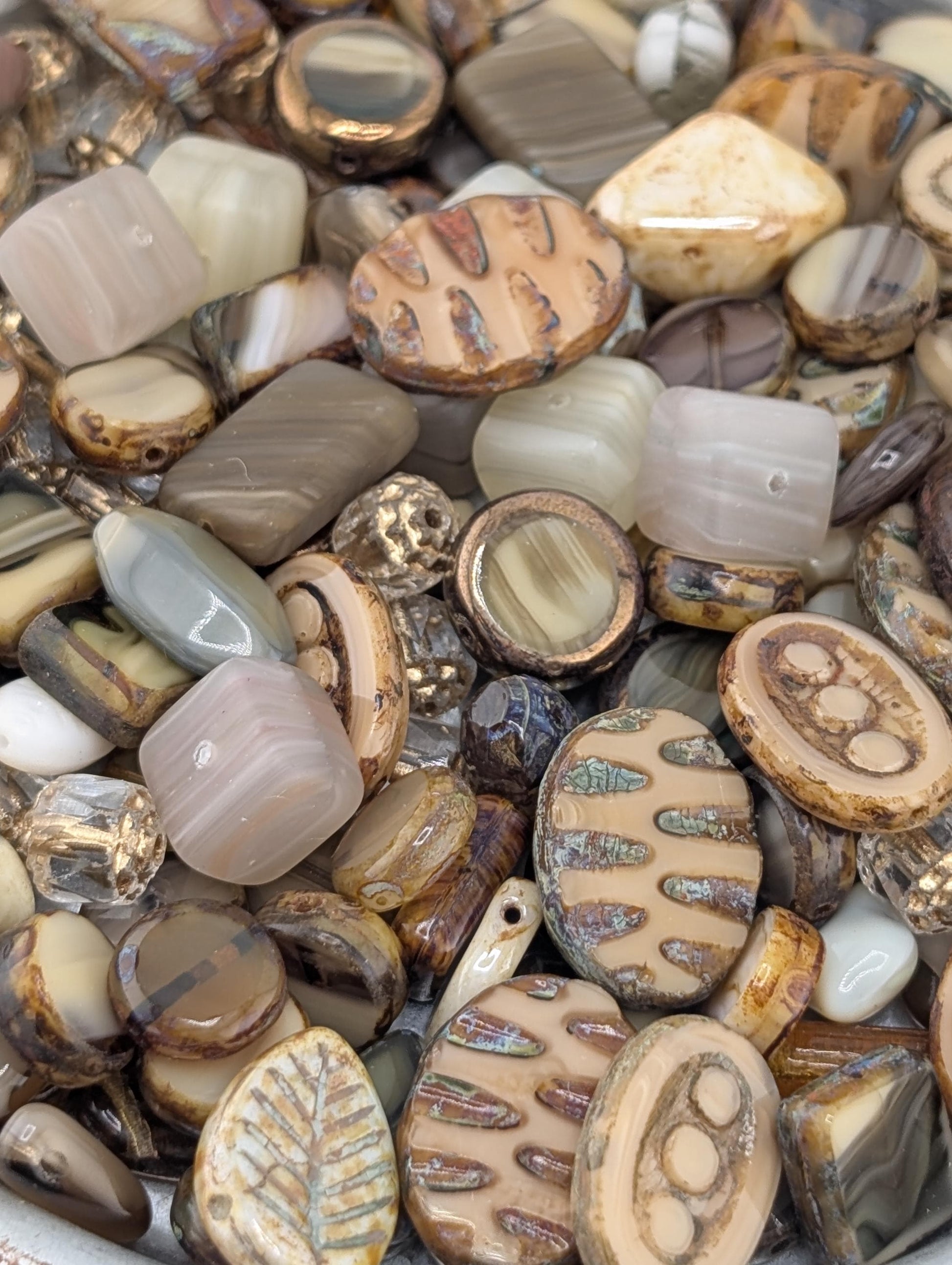 The image is a close-up of a collection of various beads and stones, including glass beads and stones in different shapes, sizes, and colors.