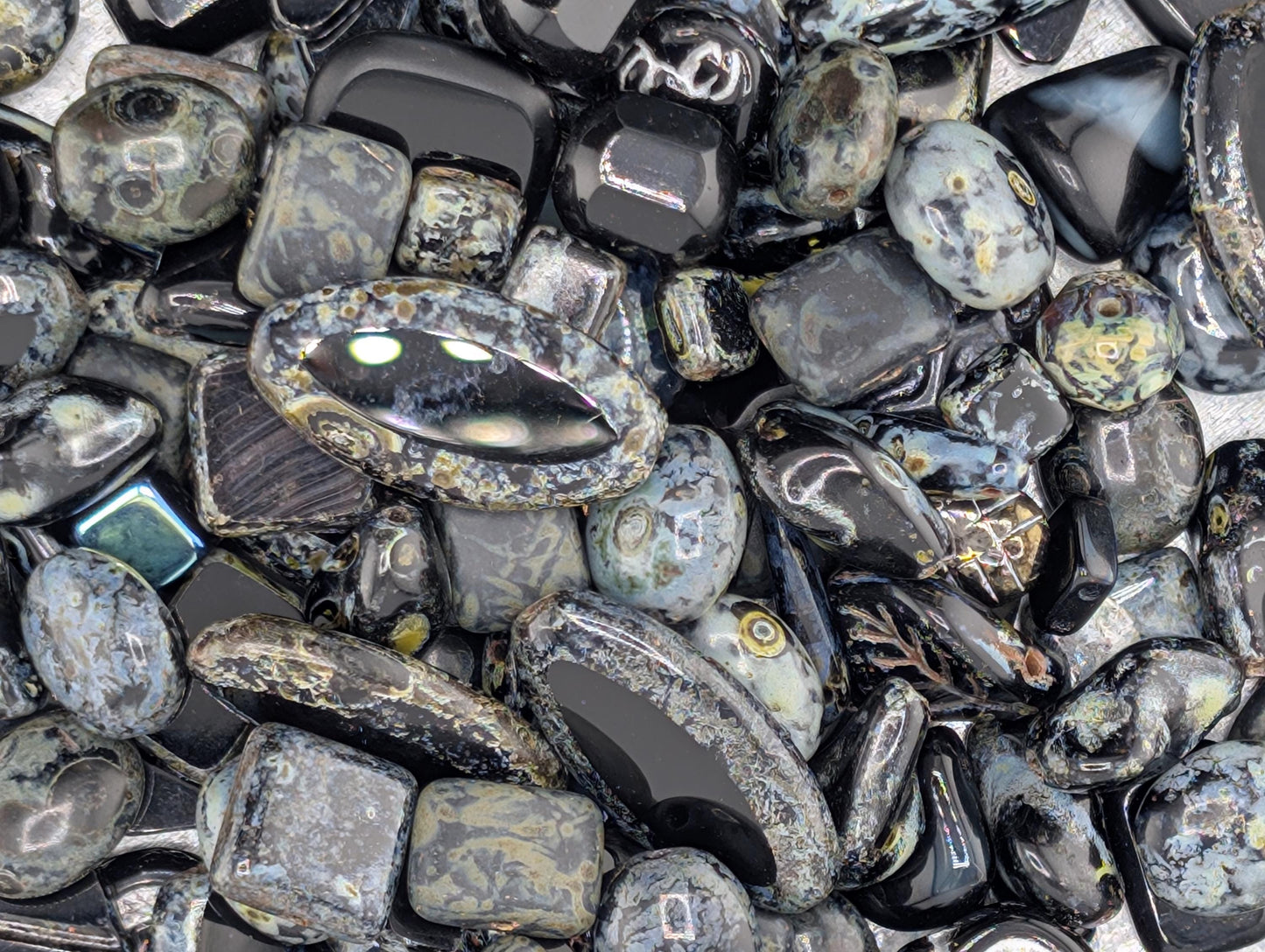The image is a close-up of various black and gray stones, including gemstones and minerals, arranged in a visually appealing manner.