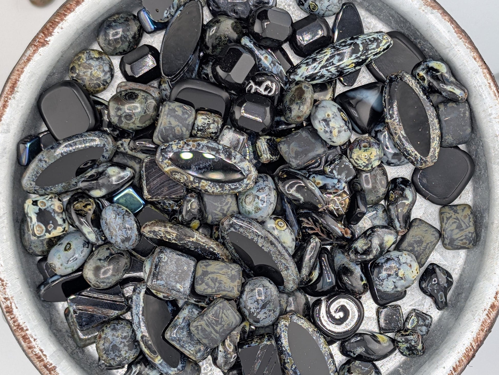 a collection of various black and gray stones, including gemstones and crystals, arranged in a bowl or container.
