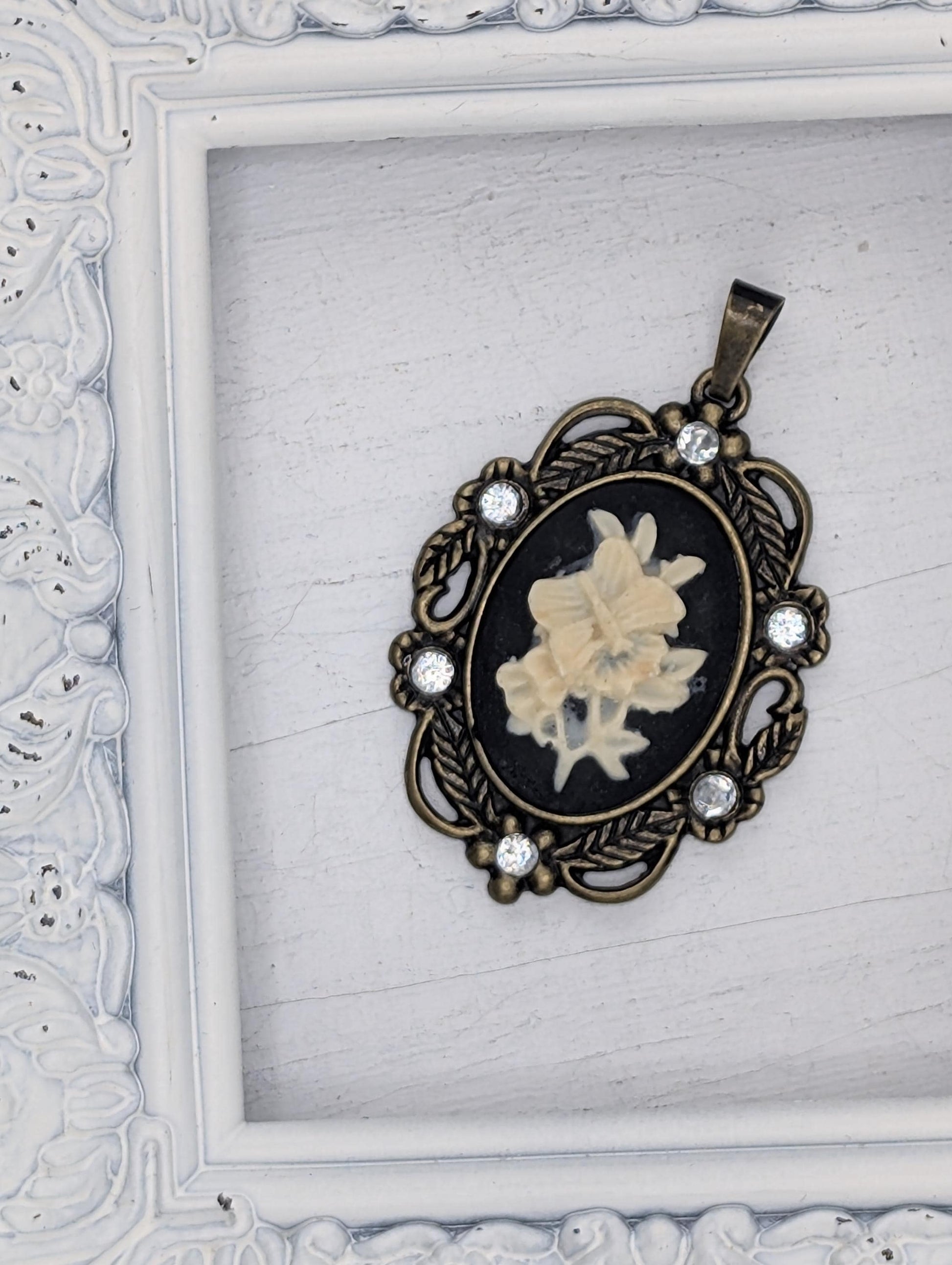 A decorative pendant featuring a floral design is displayed in a white ornate frame.