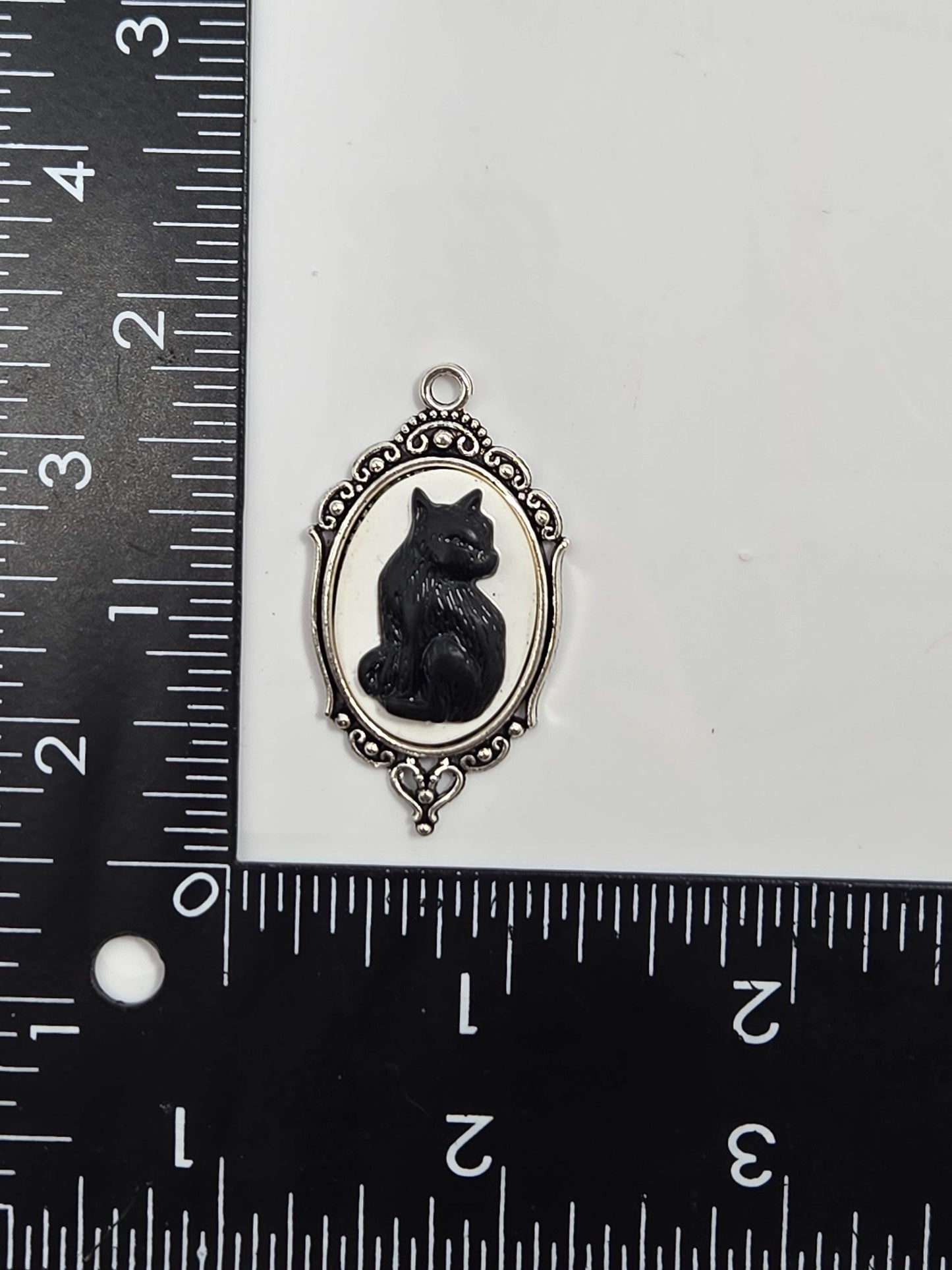 a small, ornate charm in the shape of a cat, placed next to a ruler for size comparison.