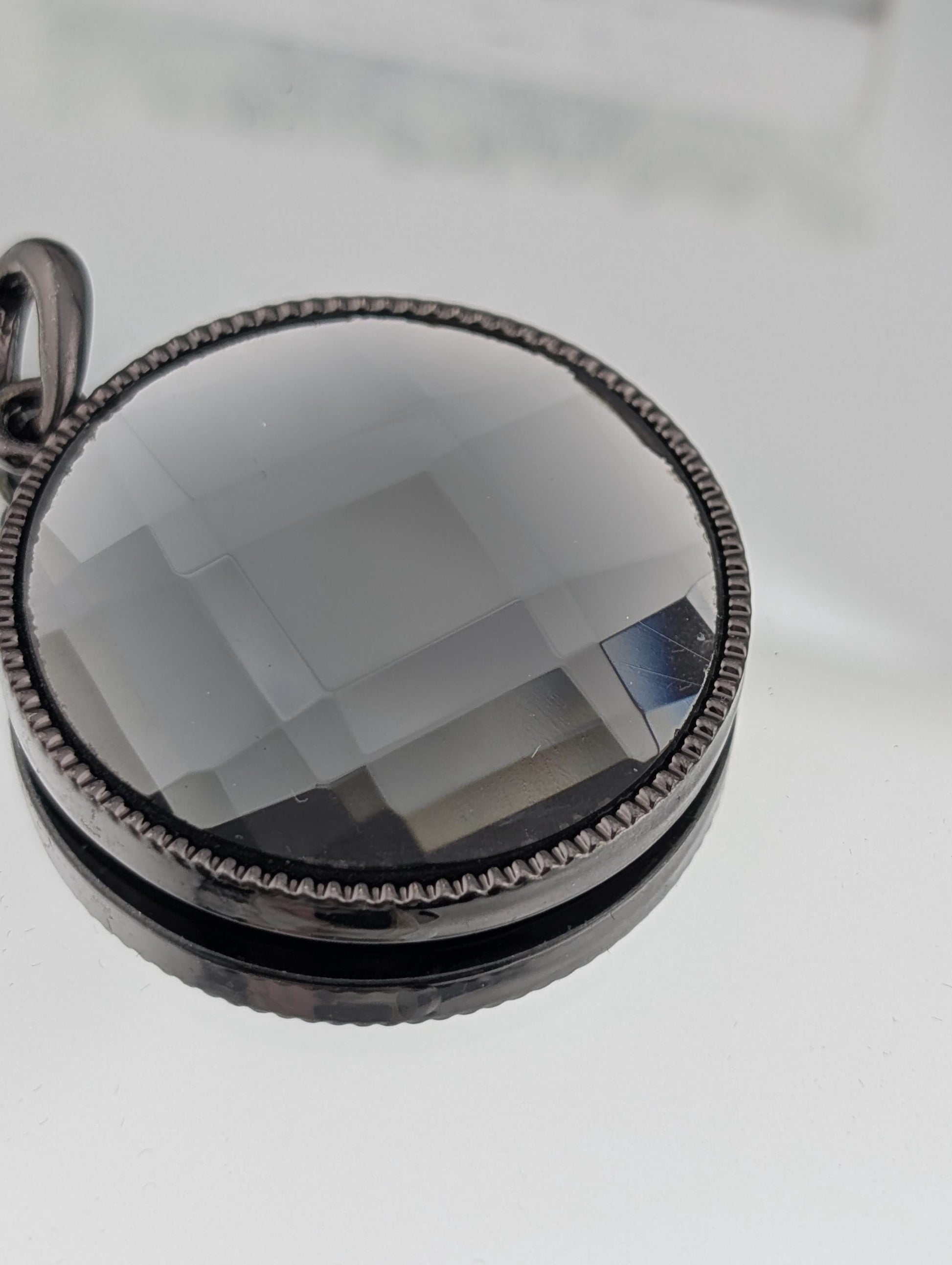 A close-up view of a round, black, and silver pendant with a clear, multicolored glass or crystal embedded in it.