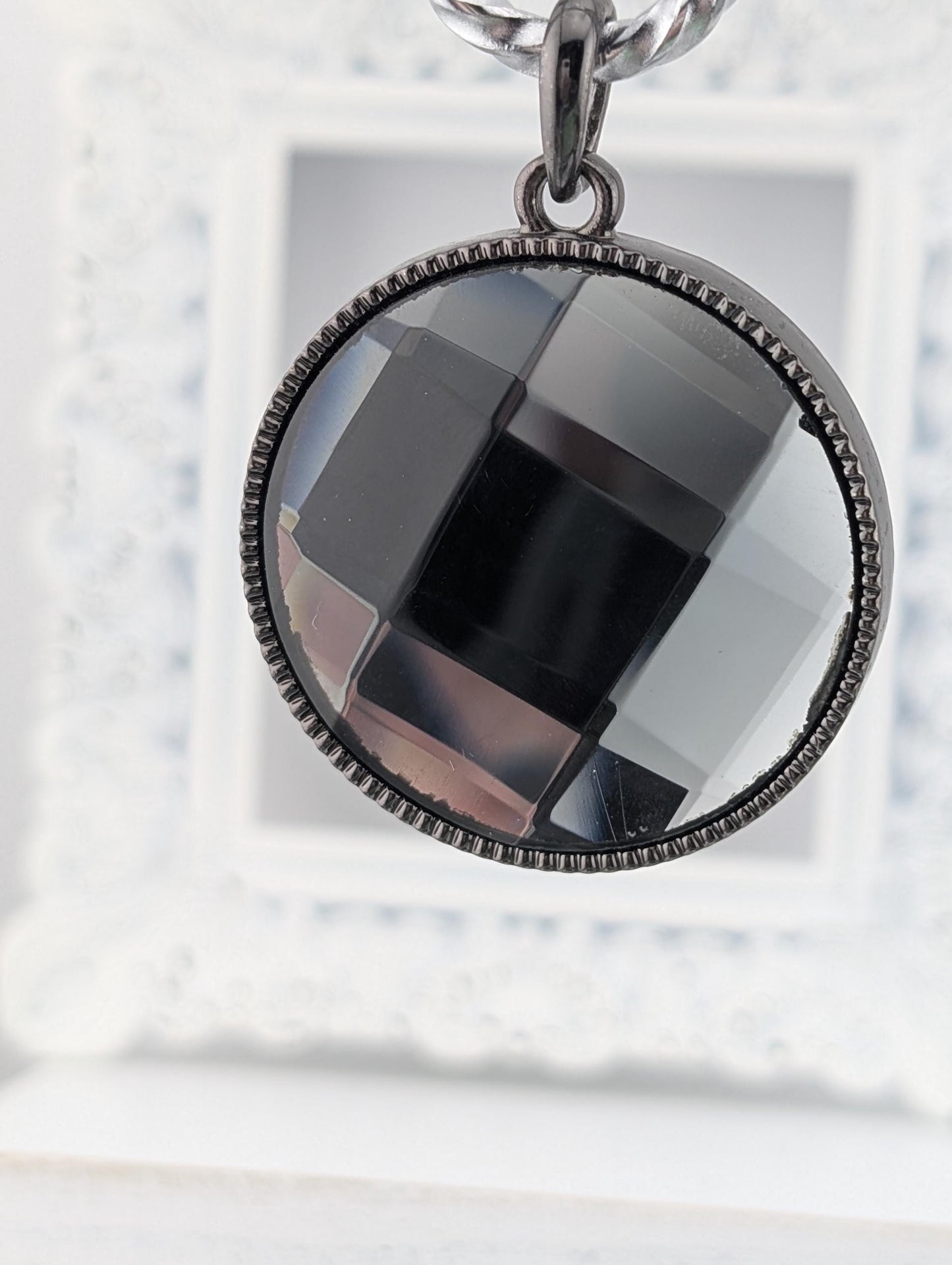 A close-up view of a circular pendant with a black and gray geometric design, hanging from a chain.